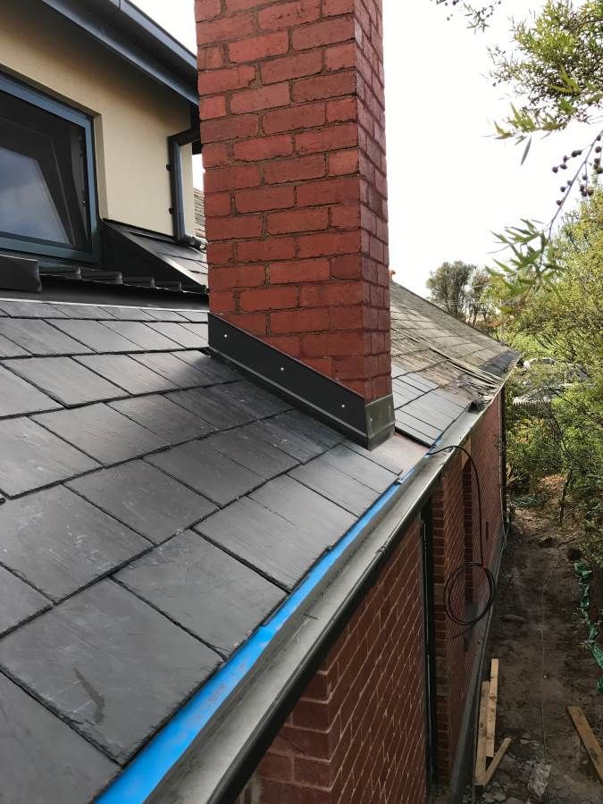 Brick chimney on a slate roof with lead flashing and a blue gutter.