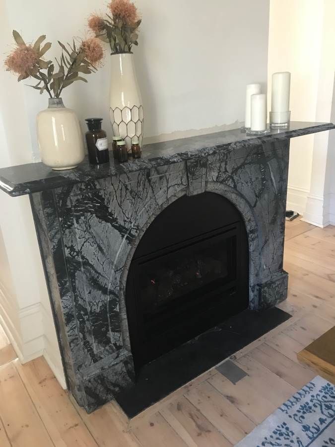 Black and gray marble fireplace with vase of flowers, candles, and bottles on the mantel.