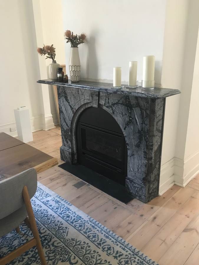 Marble fireplace with decorative candles and flowers on a mantel, set against a white wall.