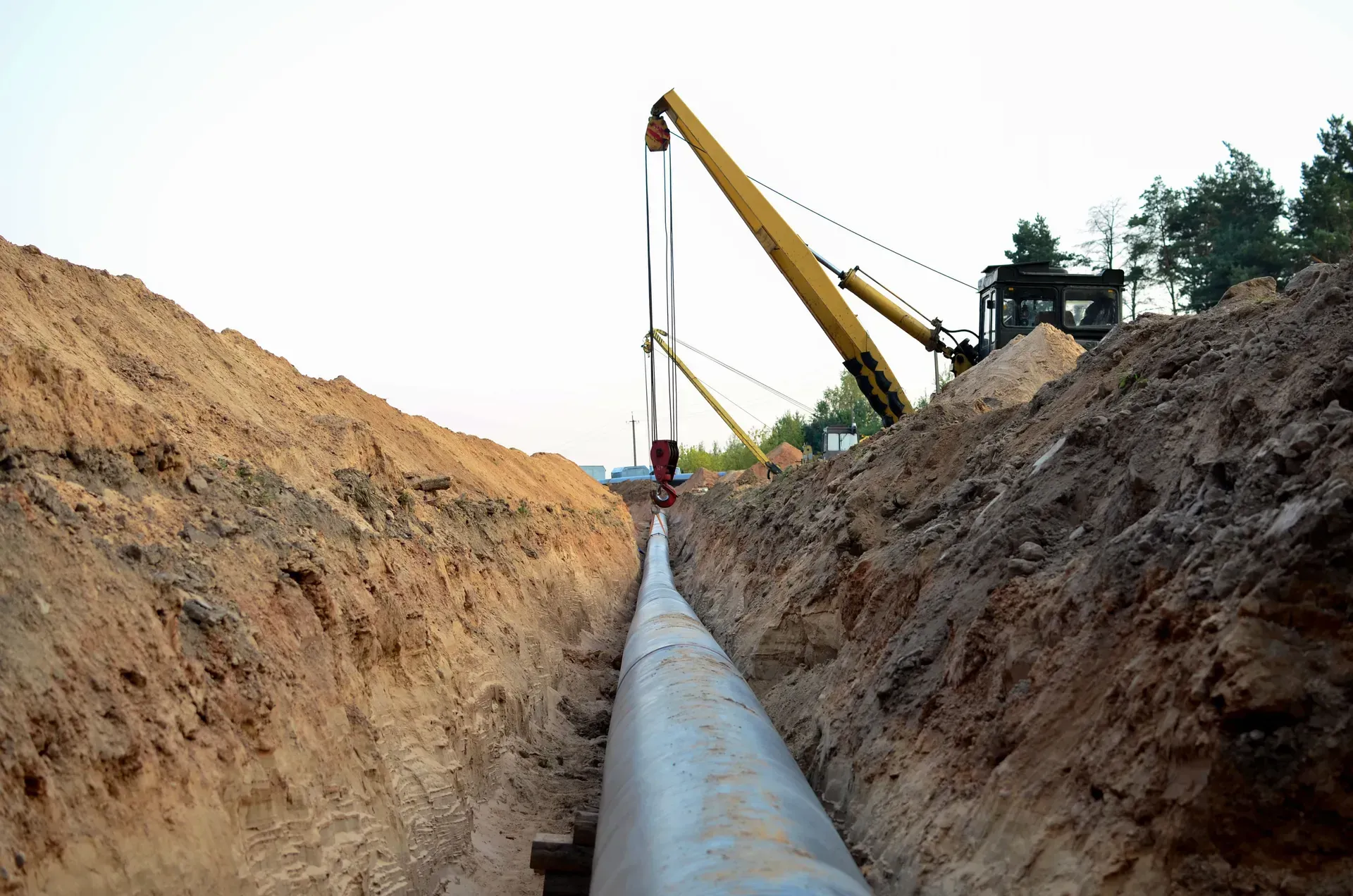 Pipeline being laid in a dirt trench by a construction excavator