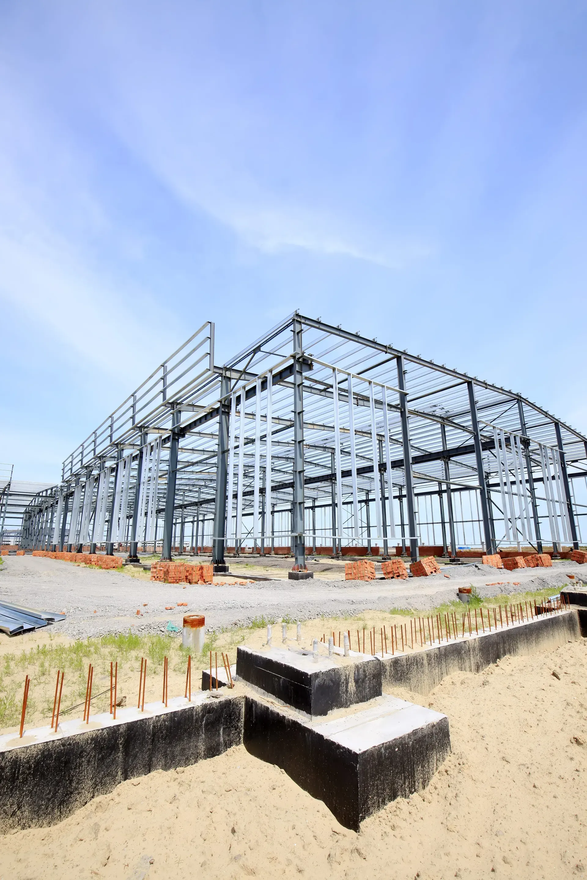 Steel frame building under construction on a gravel site under a clear blue sky