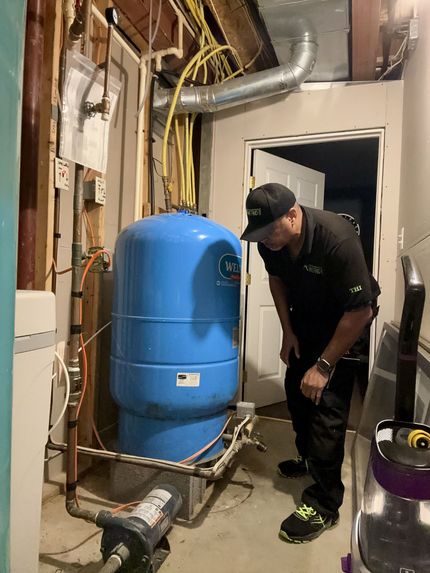 Worker inspecting blue water heater in a basement utility room