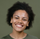 Smiling person with short curly hair against a plain green background