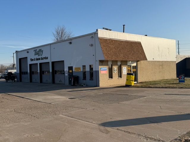 Tuffy Tire & Auto Service building with garage bays, a small office, and a paved lot under a blue sky.