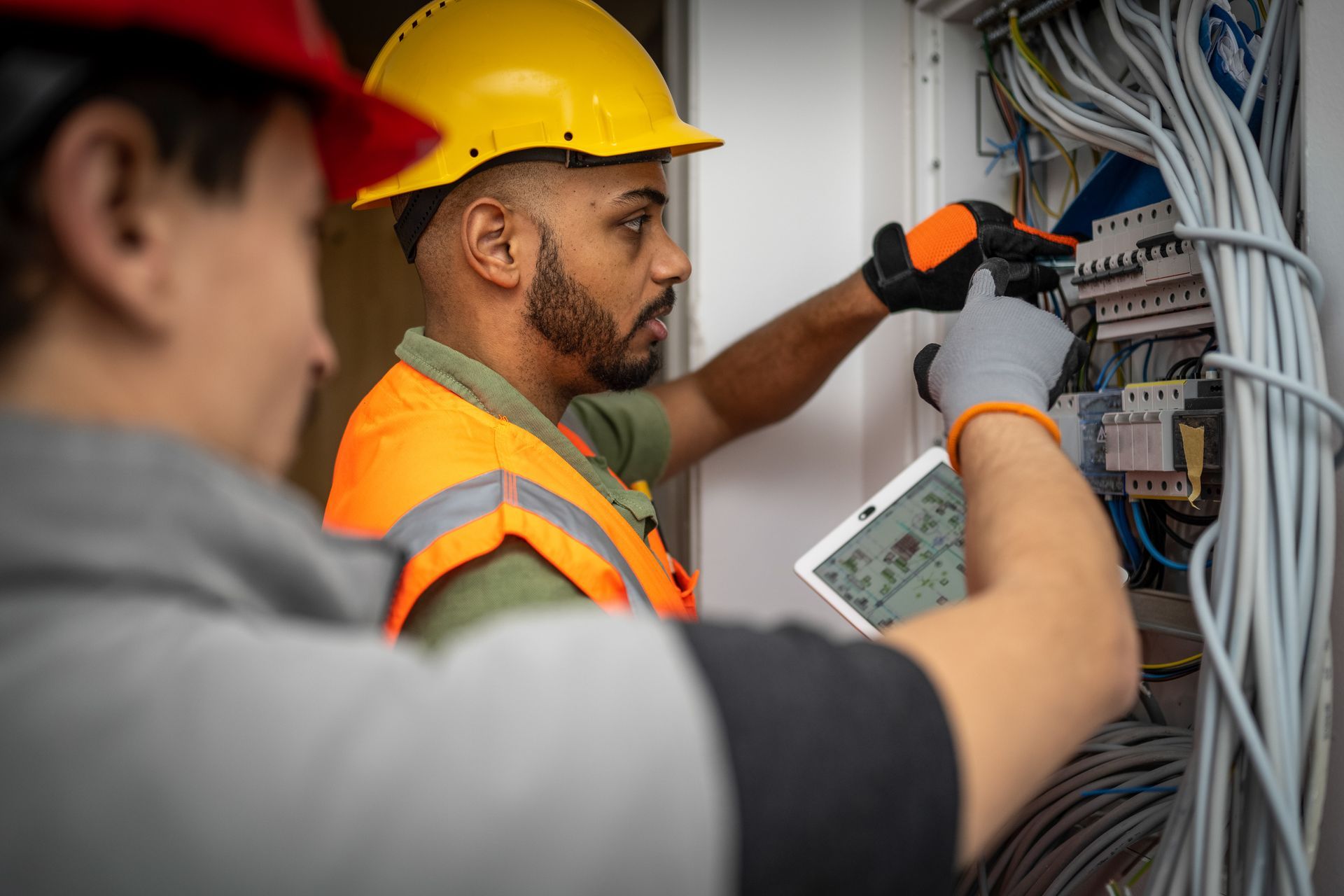 Two male electricians are working on a breaker box, providing commercial electrical services.