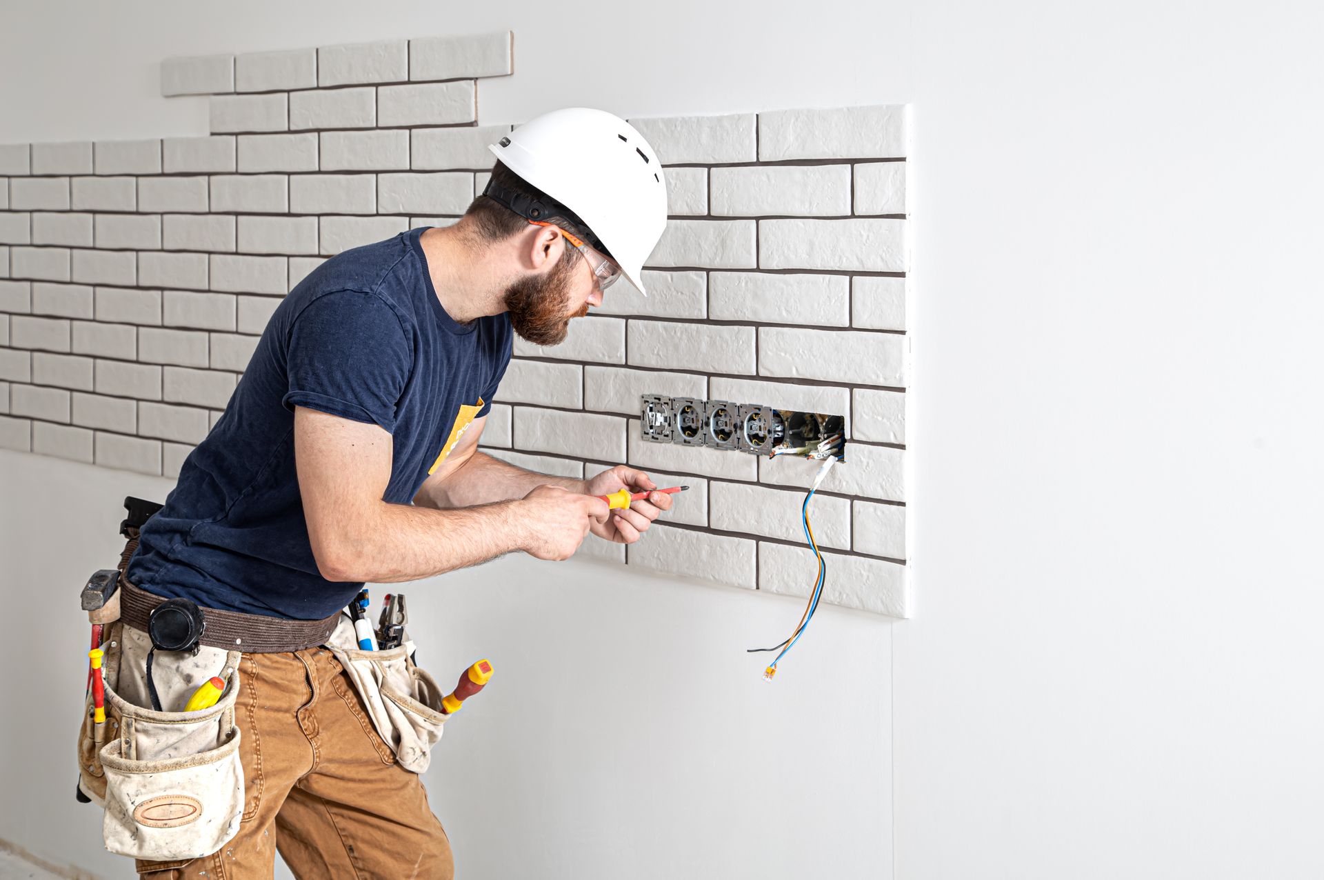 A skilled electrician wiring a brick wall outlet, offering professional electrician services. A skilled electrician wiring a brick wall outlet, offering professional electrician services.