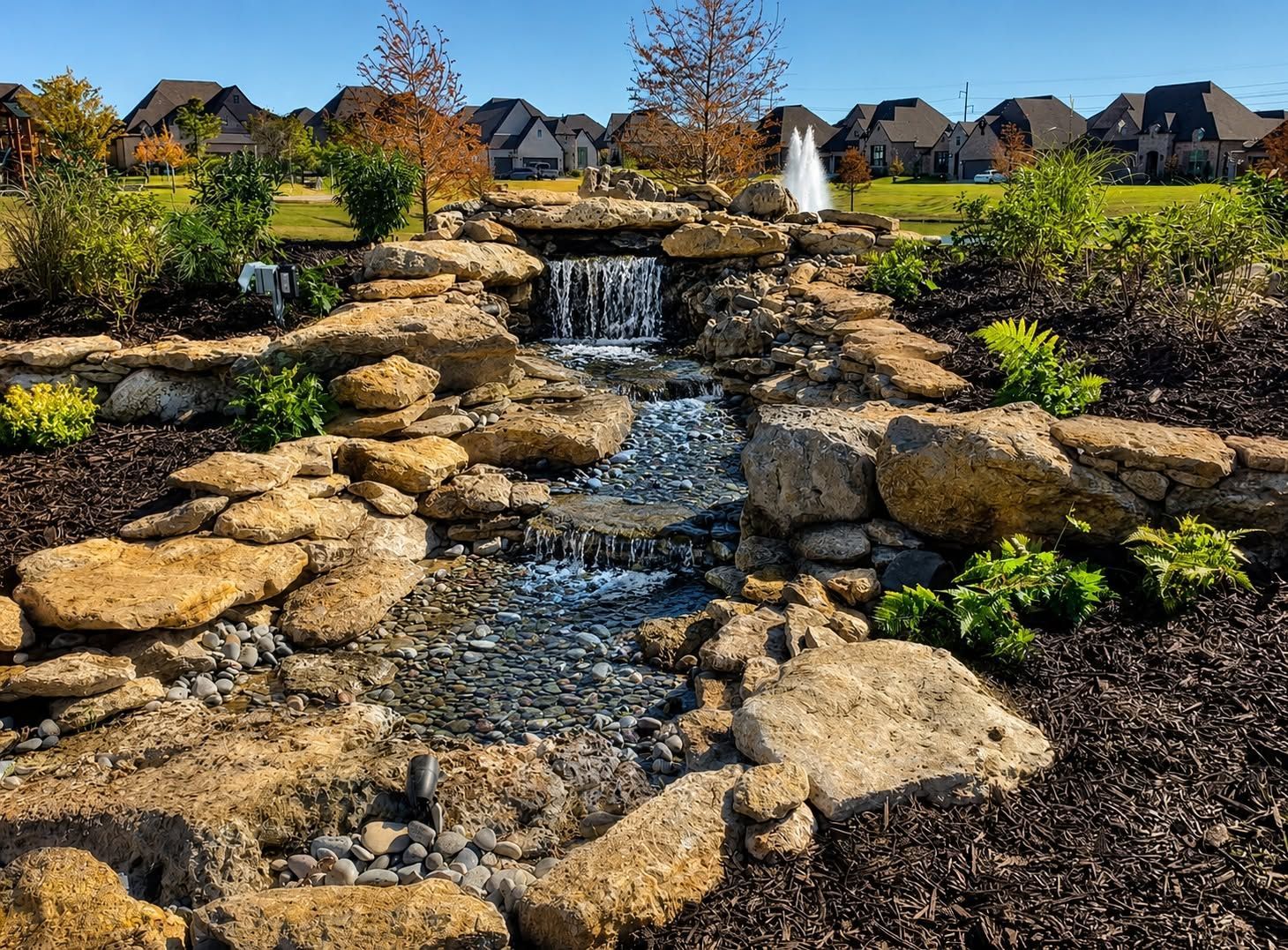 Circular rock garden with layered stones and small shrubs in a grassy suburban park under a blue sky