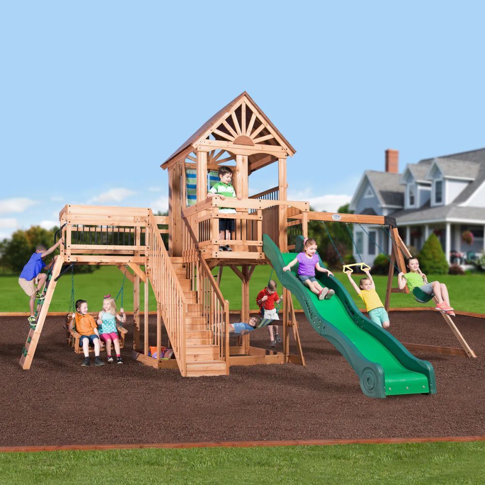 Children play on a wooden playground with a green slide and swings on a sunny day.