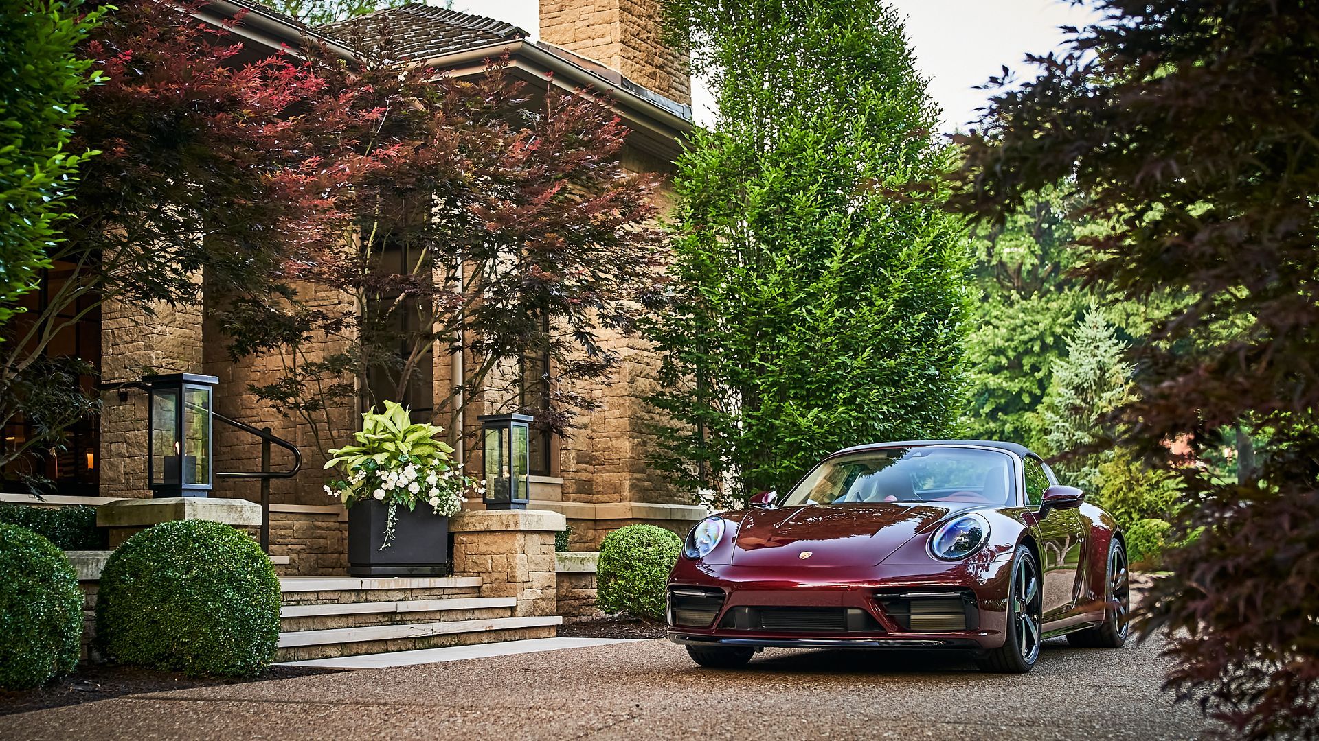 A red sports car is parked in front of a brick house.