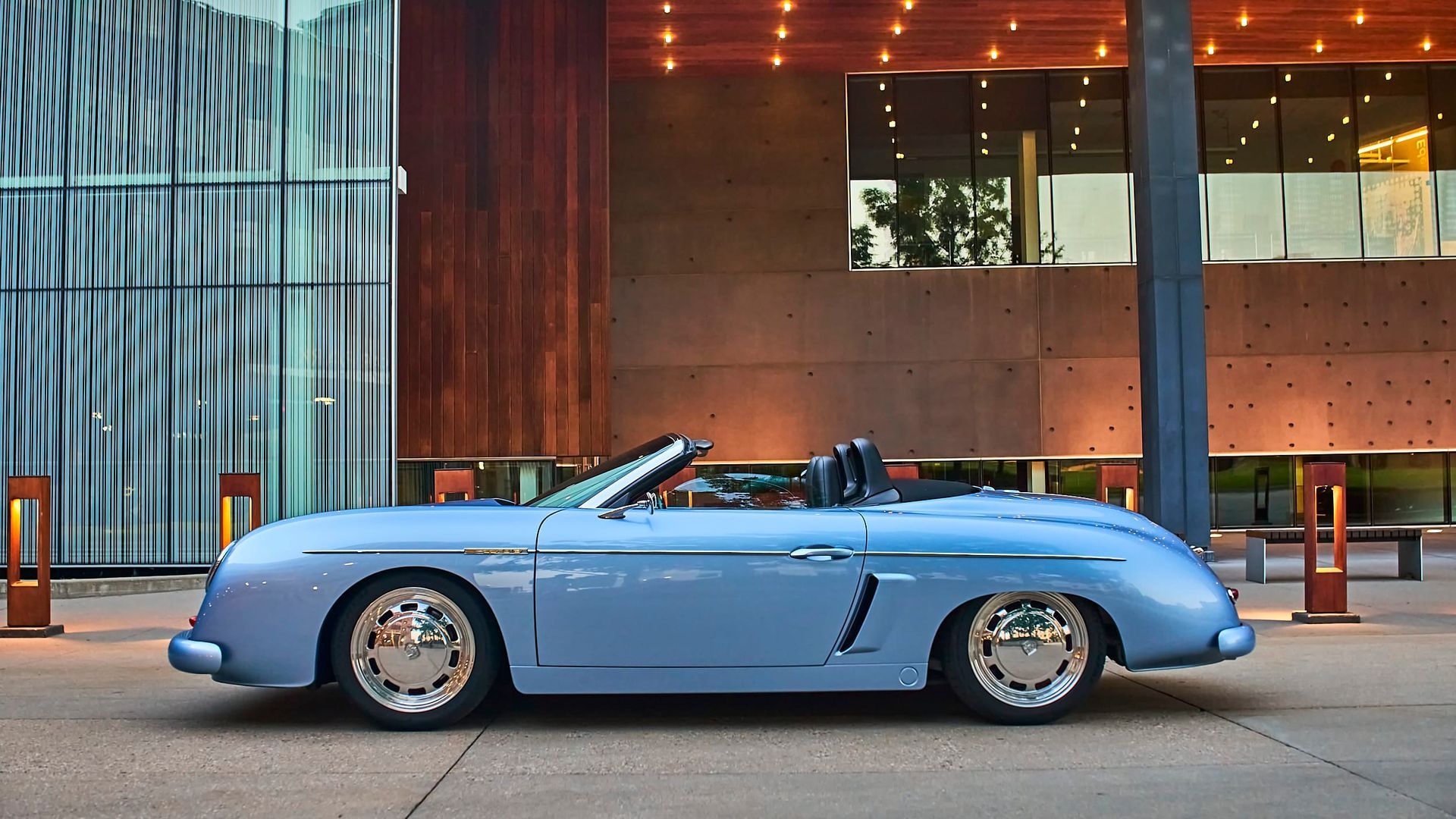 Light blue convertible sports car parked outside a modern building with glass and wood paneling.