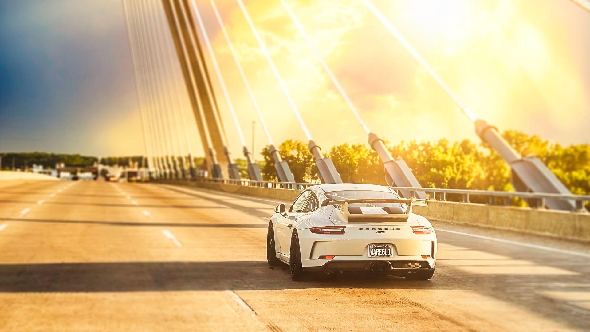 A white sports car is driving down a highway at sunset.