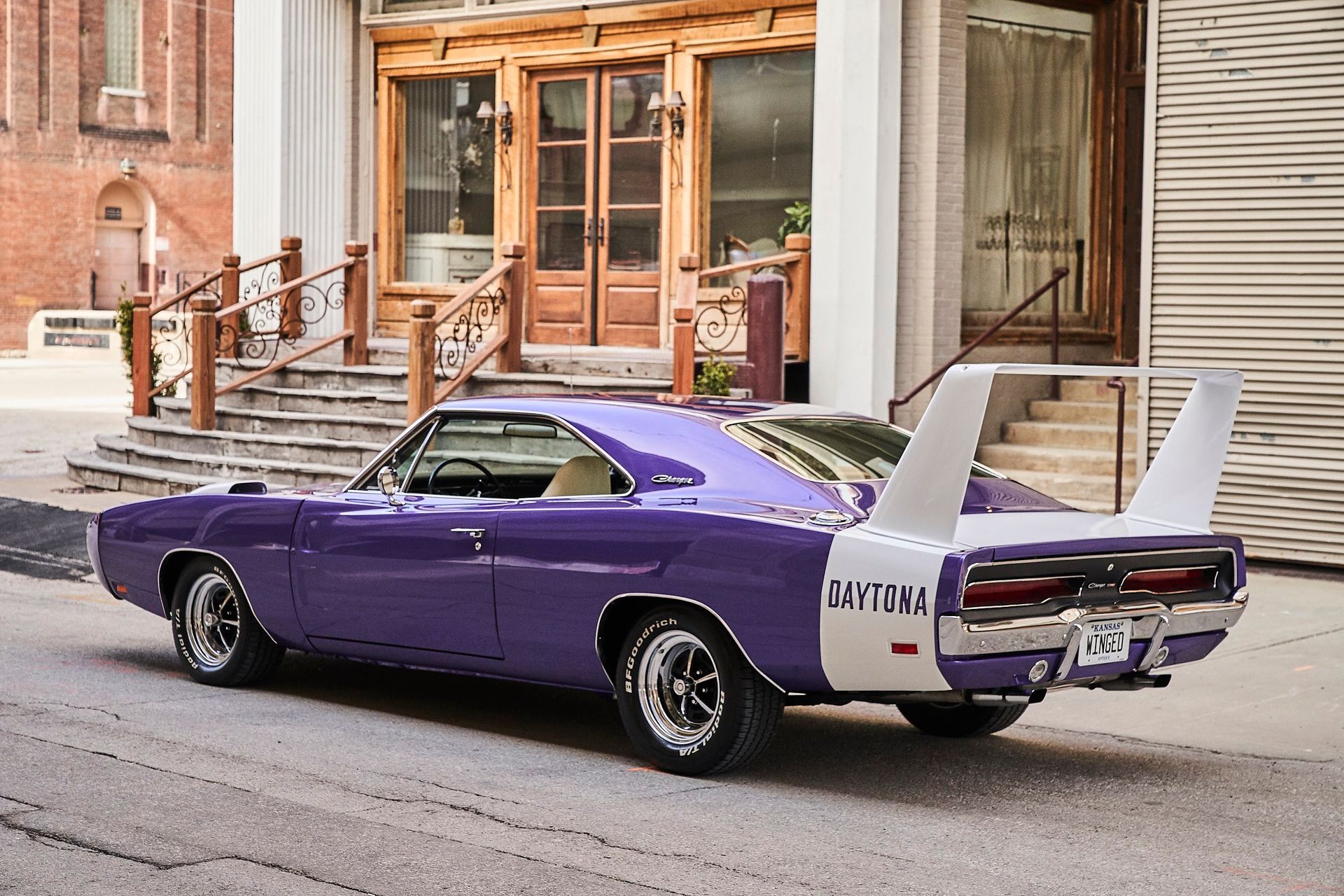 A purple and white dodge charger is parked on the side of the road in front of a building.