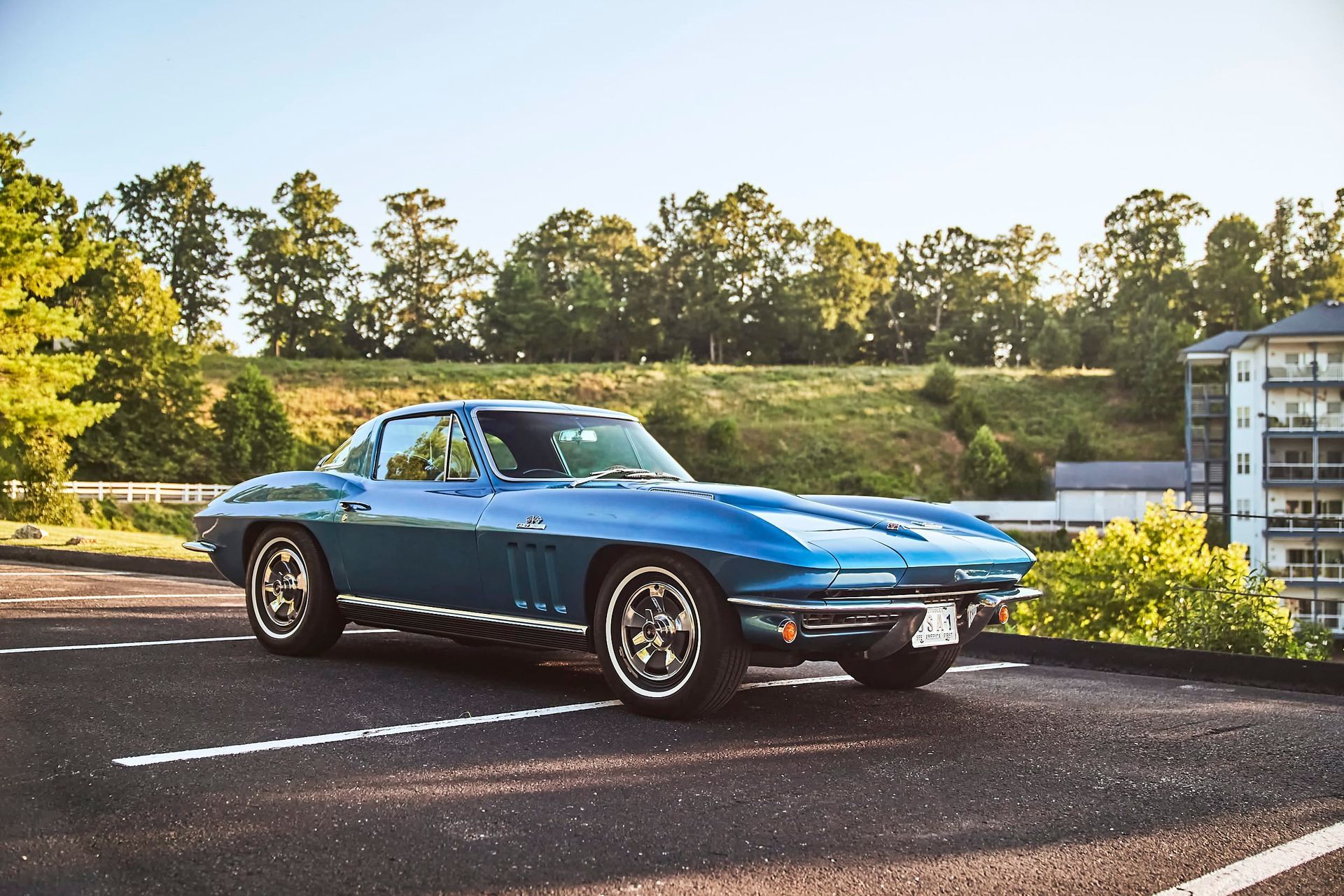 Blue classic Corvette parked outside on a sunny day, with trees and a building in the background.