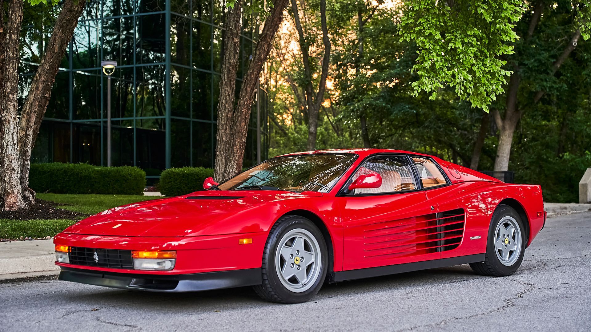 A red ferrari testarossa is parked on the side of the road.