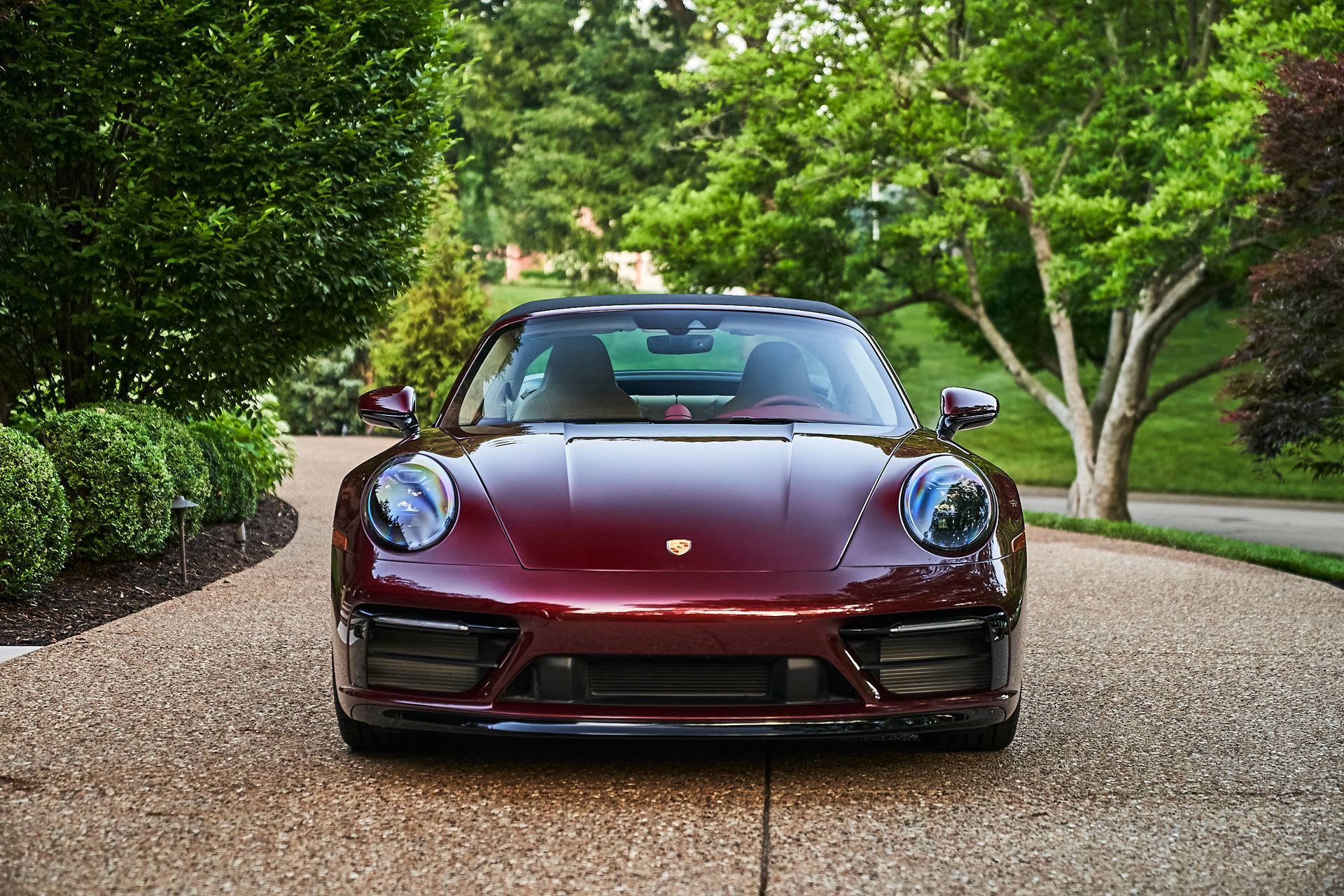 A red porsche 911 is parked in a driveway surrounded by trees.