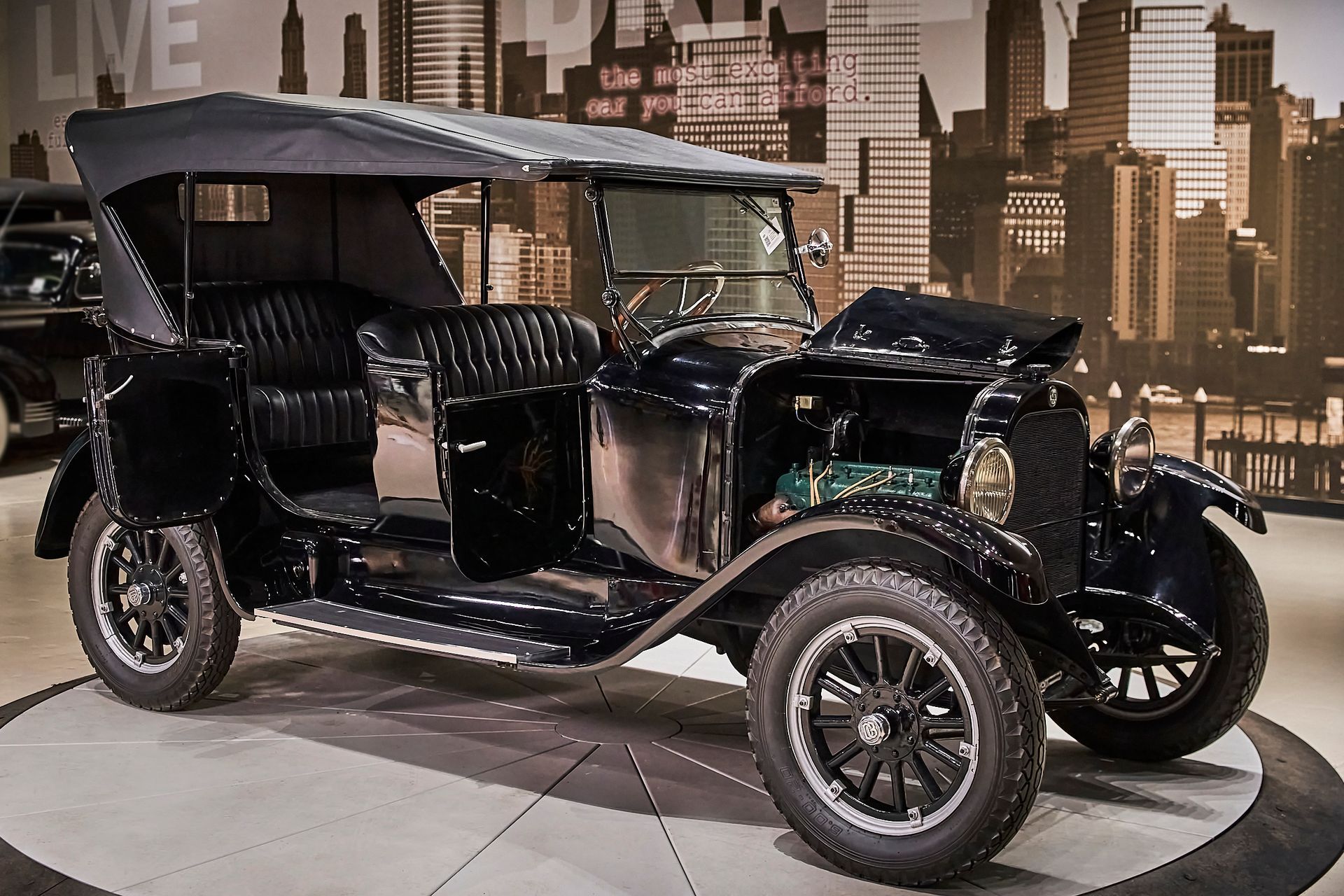 An old black car is parked in front of a sign that says live