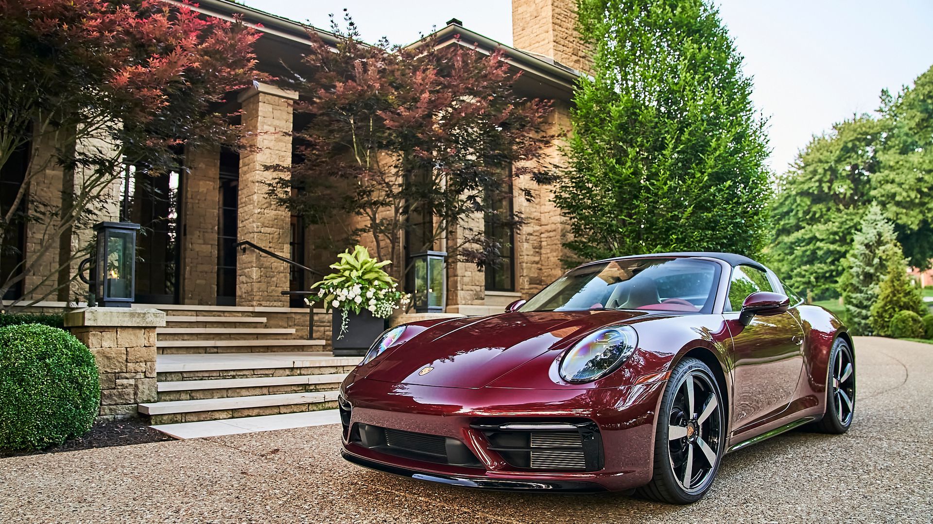 A red porsche 911 is parked in front of a house.