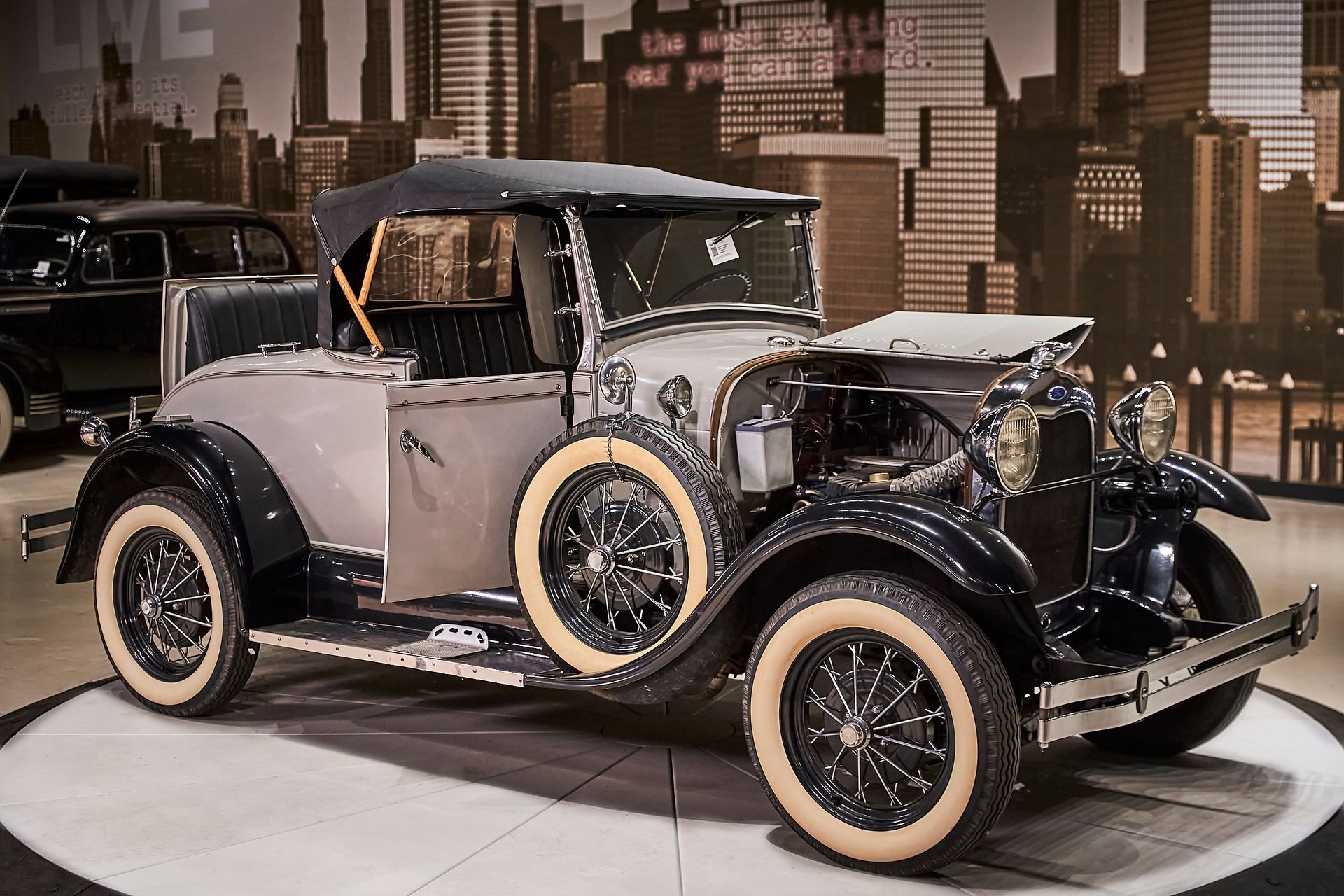 An old fashioned car is parked in front of a city skyline
