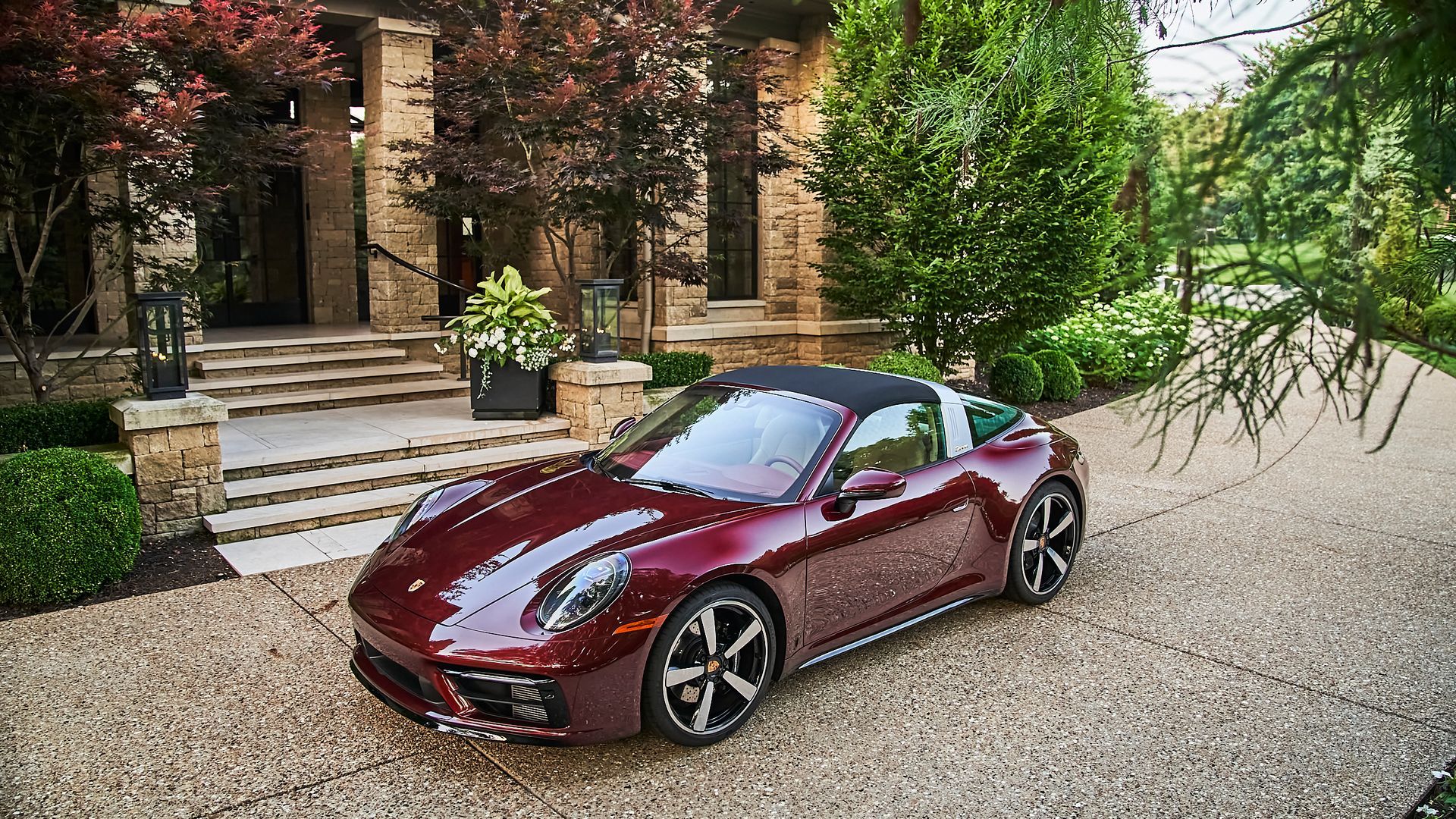A red porsche targa is parked on a gravel driveway in front of a house.