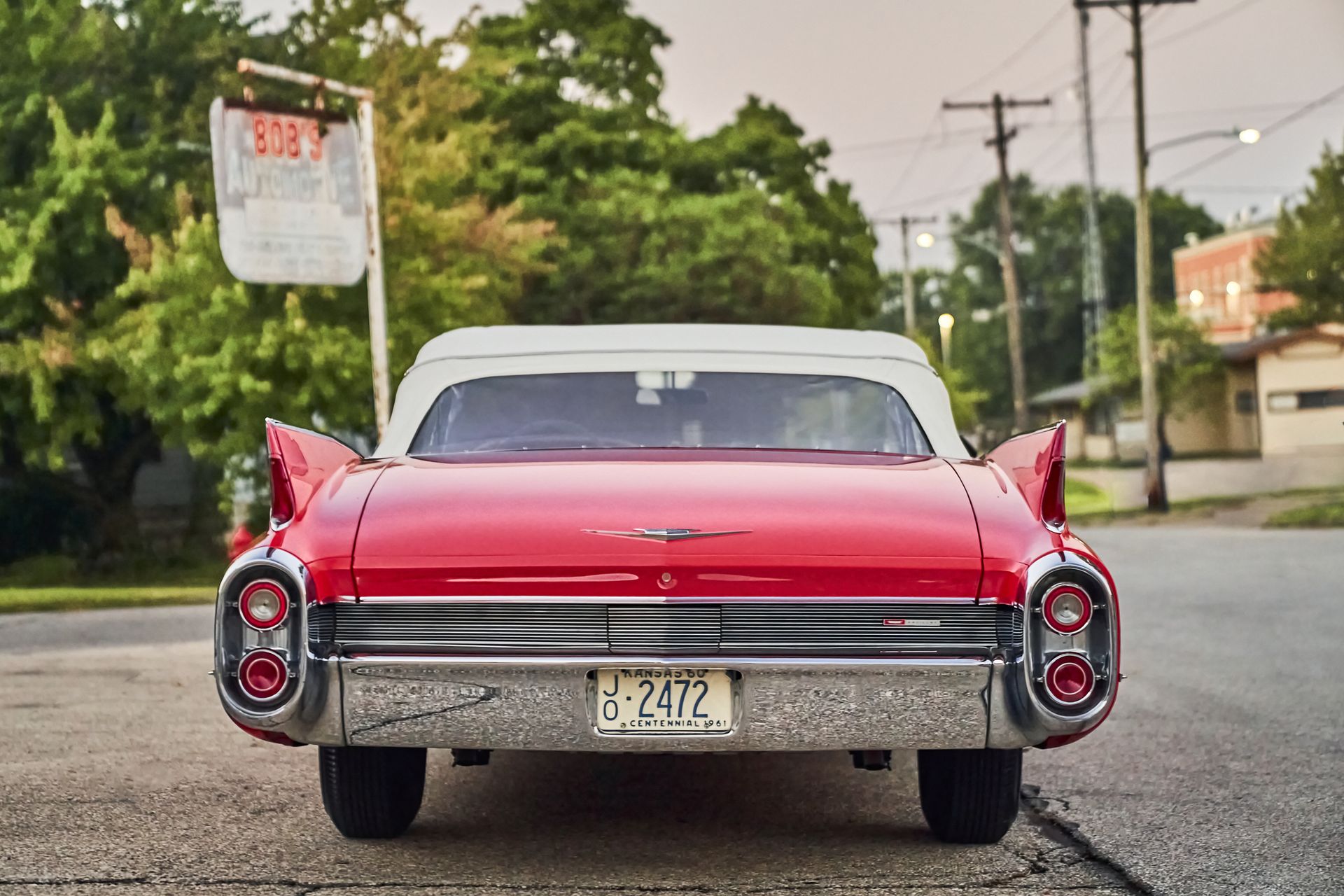 A red and white car is parked on the side of the road in front of a gas station.