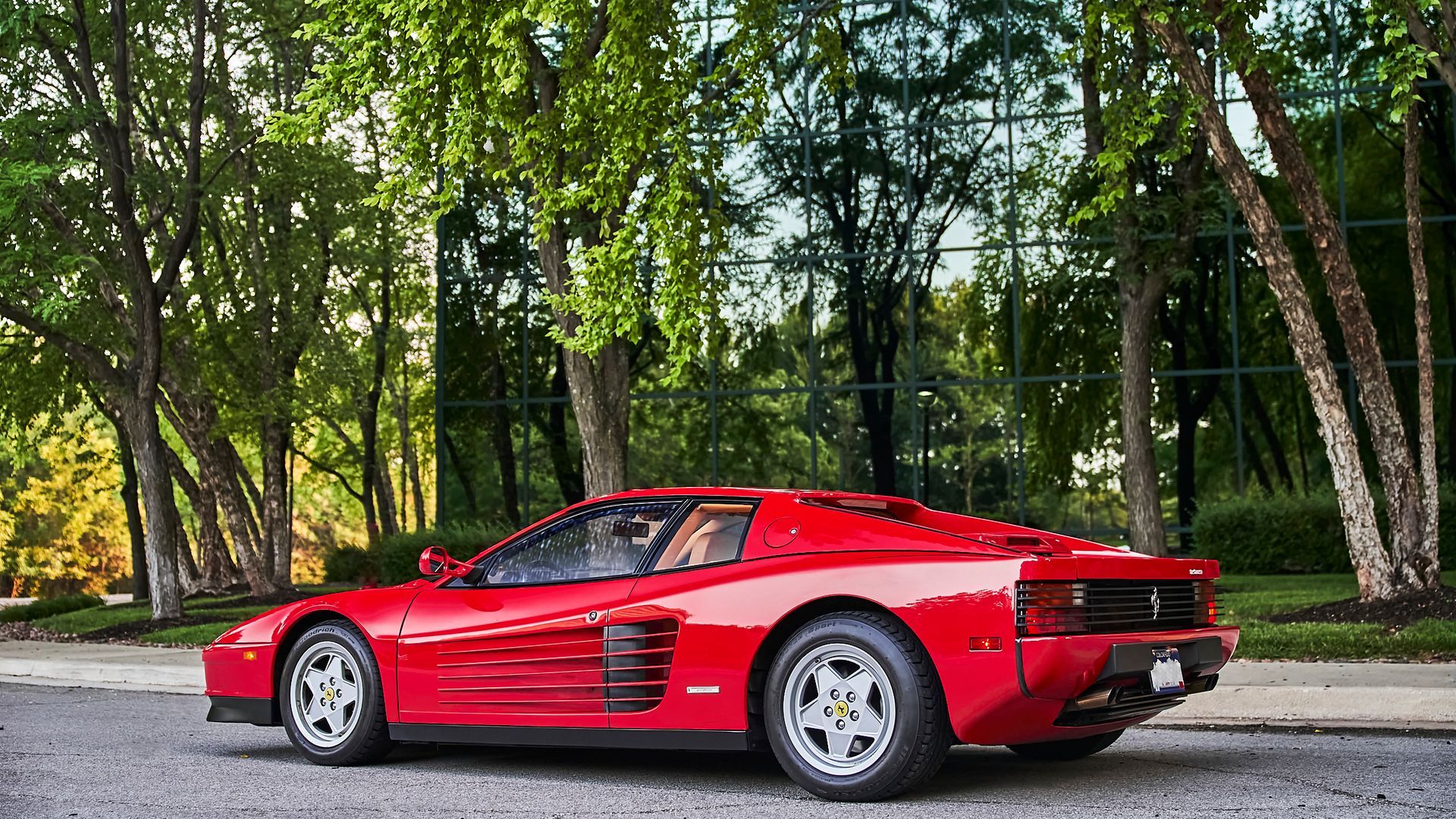 A red ferrari testarossa is parked on the side of the road in front of trees.