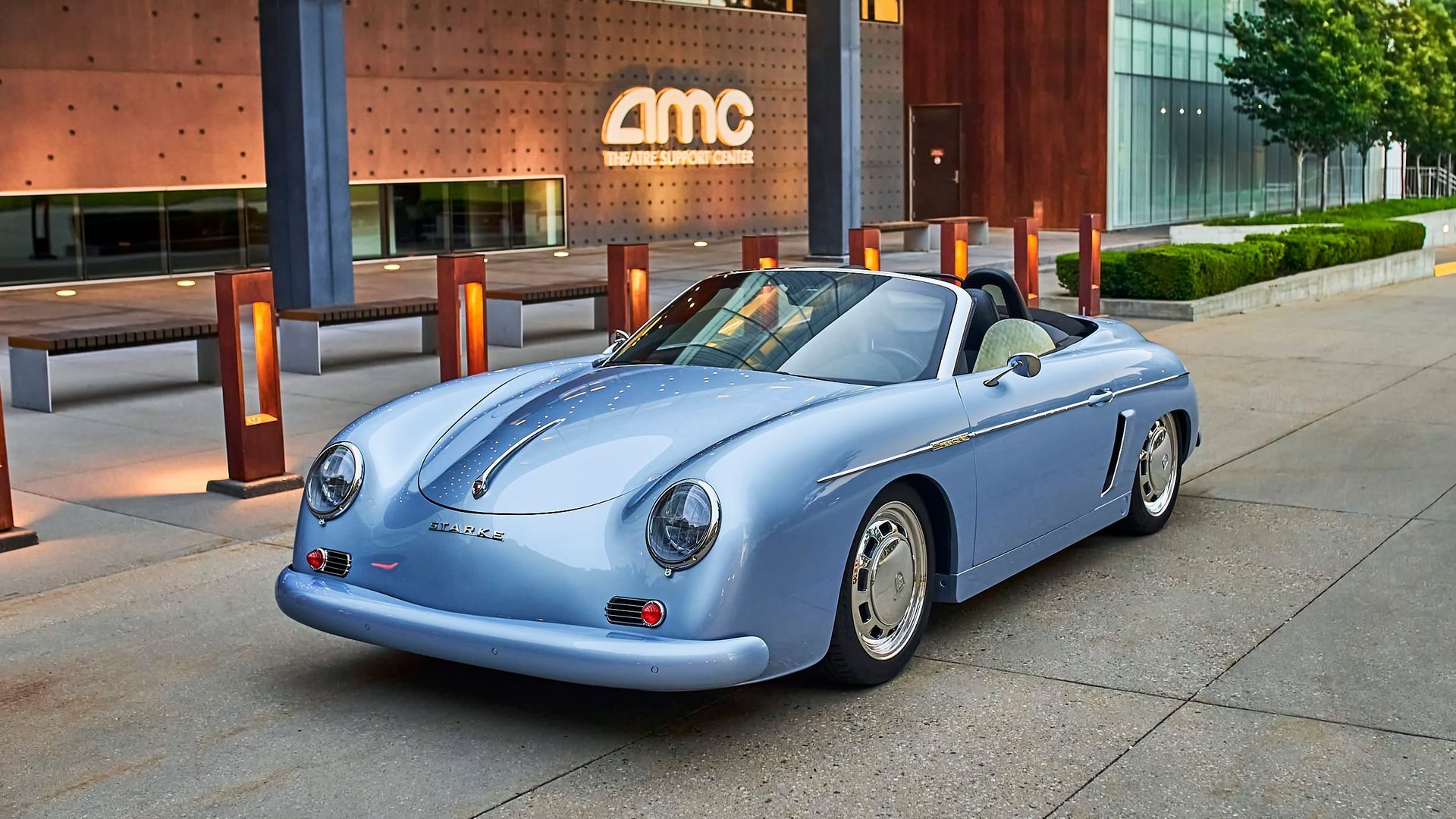 An ice blue Porsche Speedster is parked in a driveway in front of a corporation.