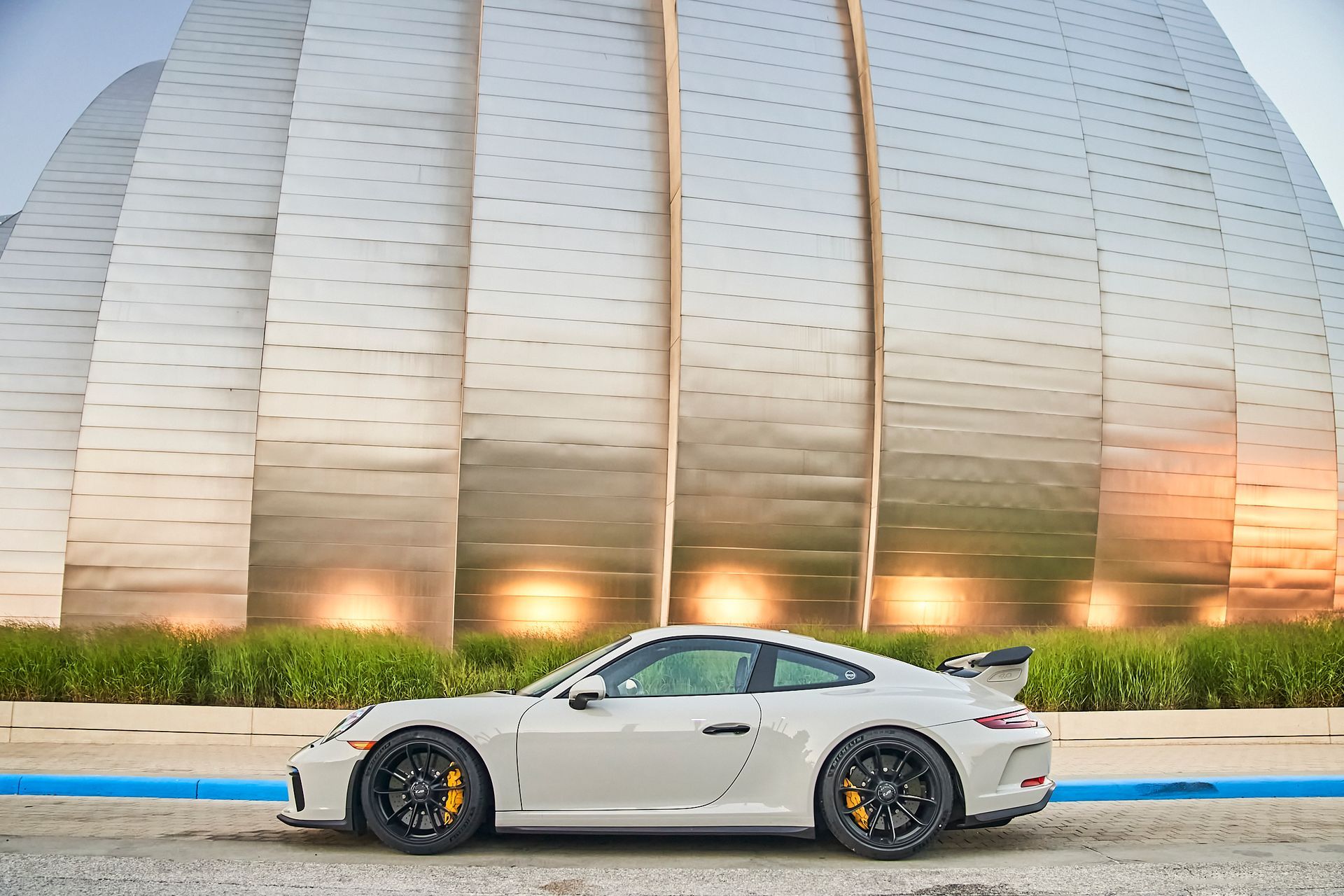 A white porsche 911 gt3 is parked in front of a large building.