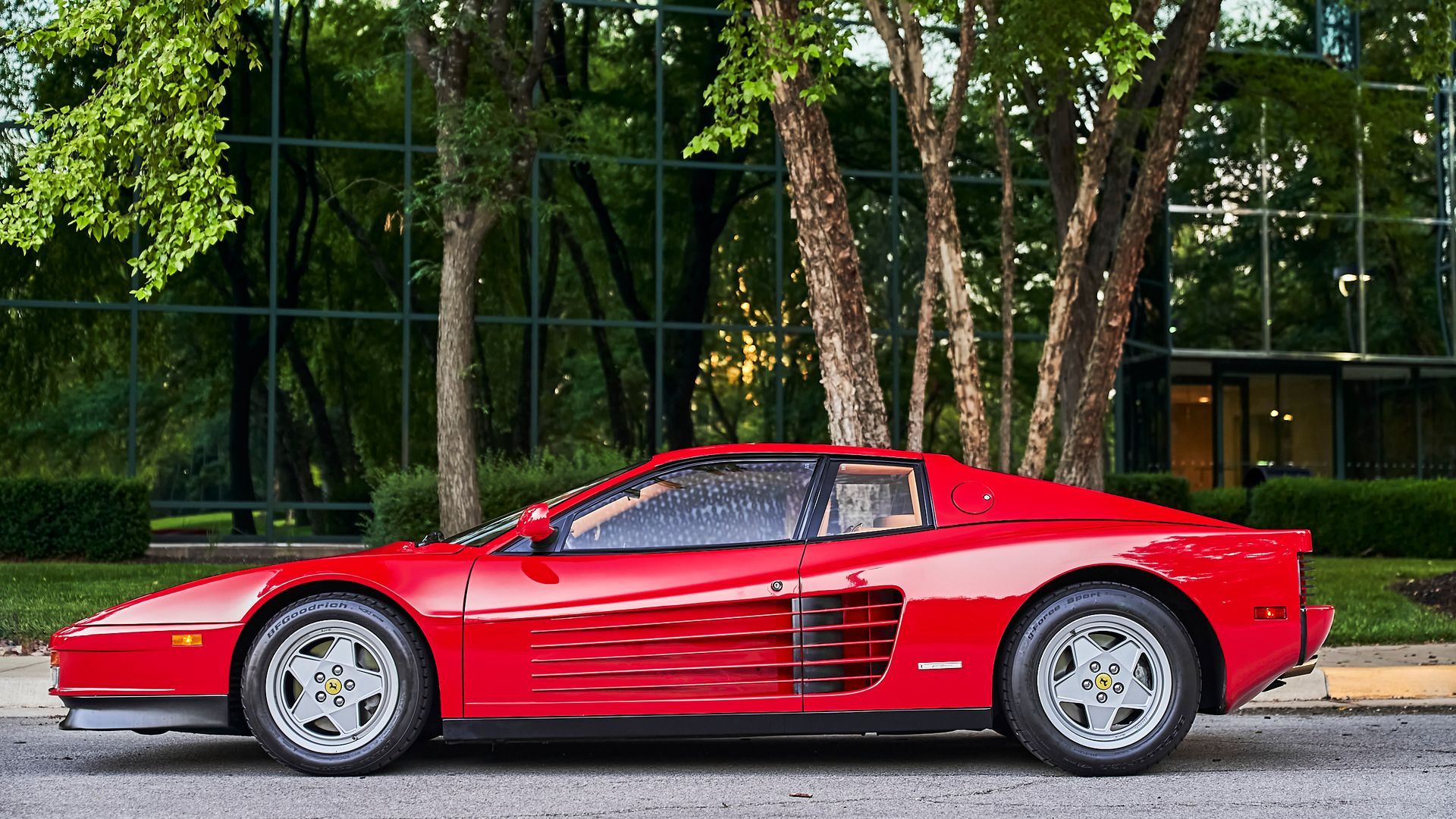A red ferrari testarossa is parked on the side of the road in front of a building.