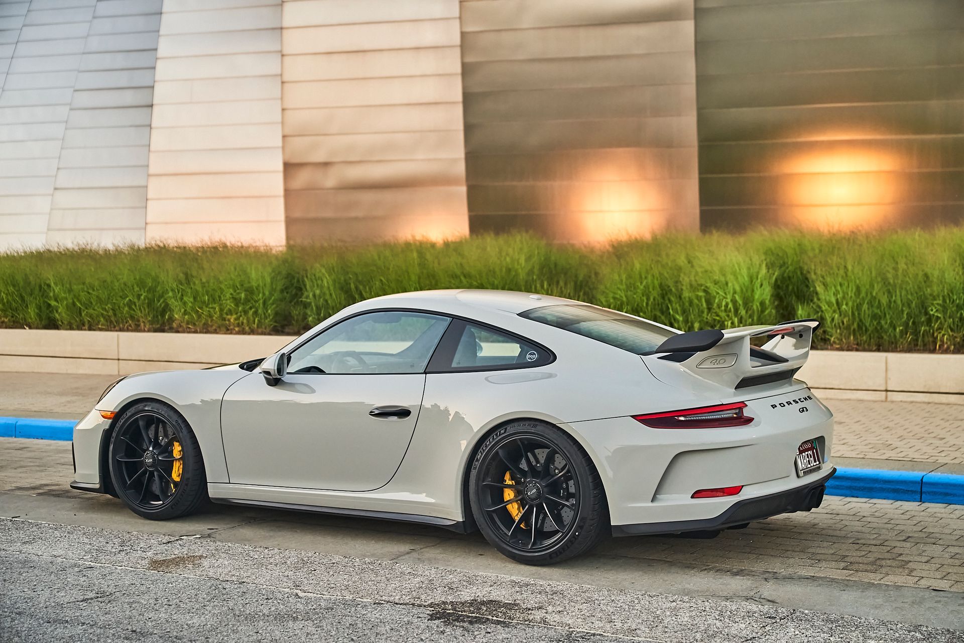 A white porsche 911 gt3 is parked on the side of the road in front of a building.