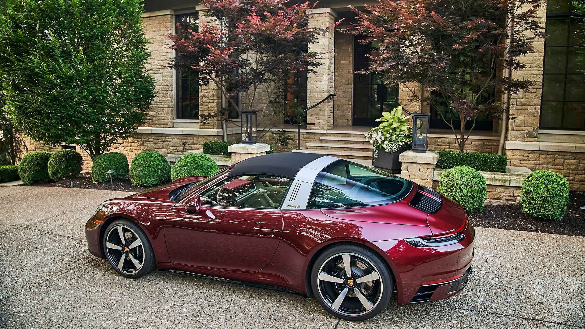 A red porsche targa is parked in front of a brick house.