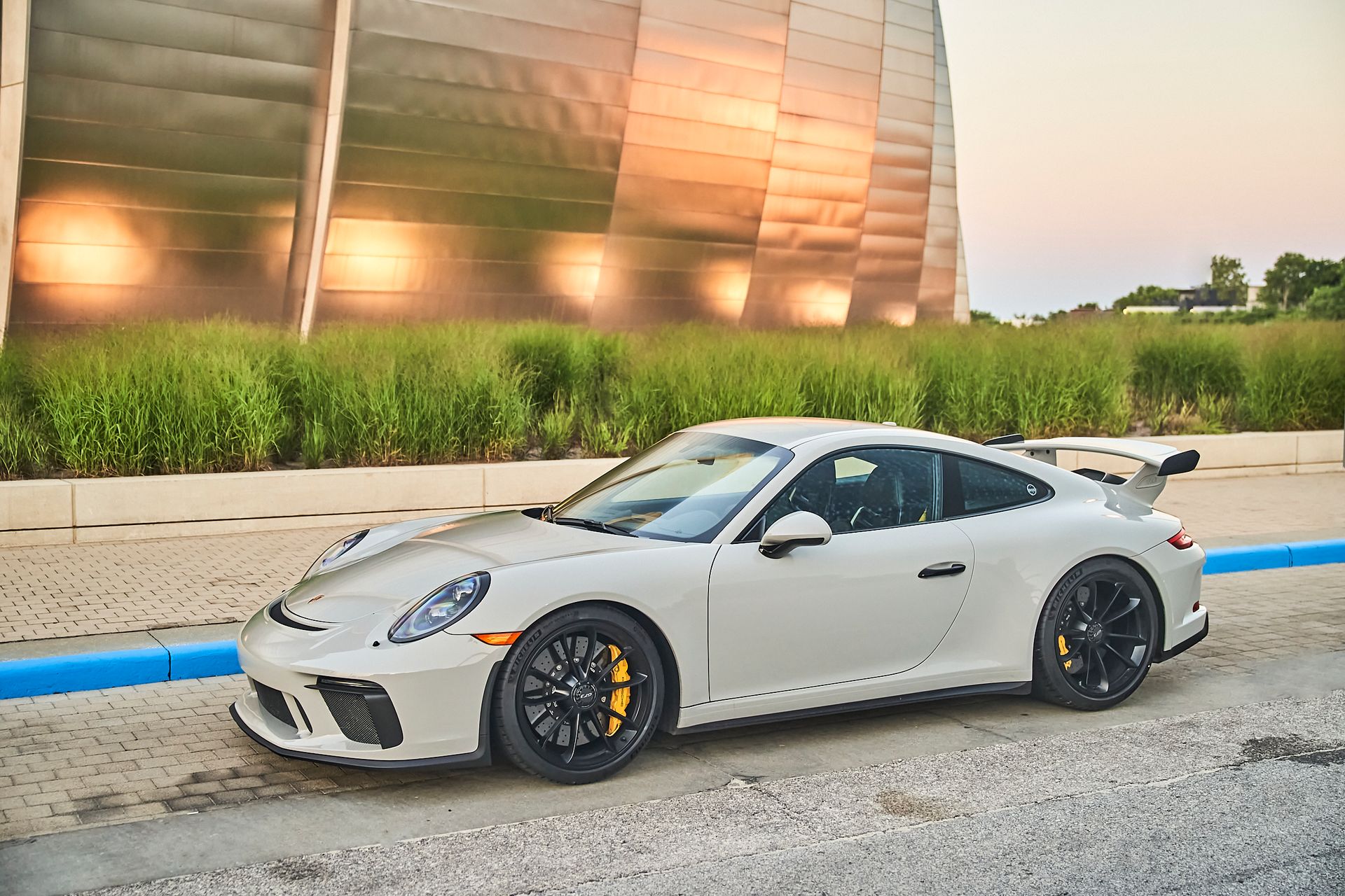 A white porsche 911 gt3 is parked in a parking lot in front of a building.