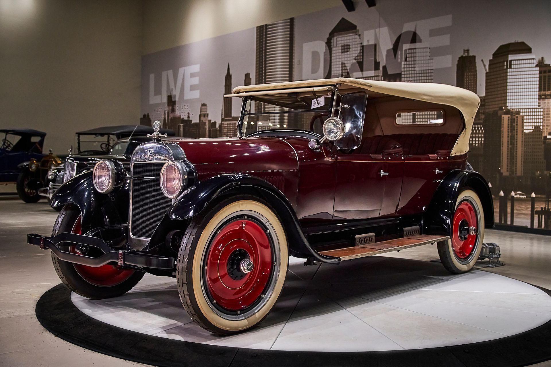 An old car is on display in front of a wall that says live drive