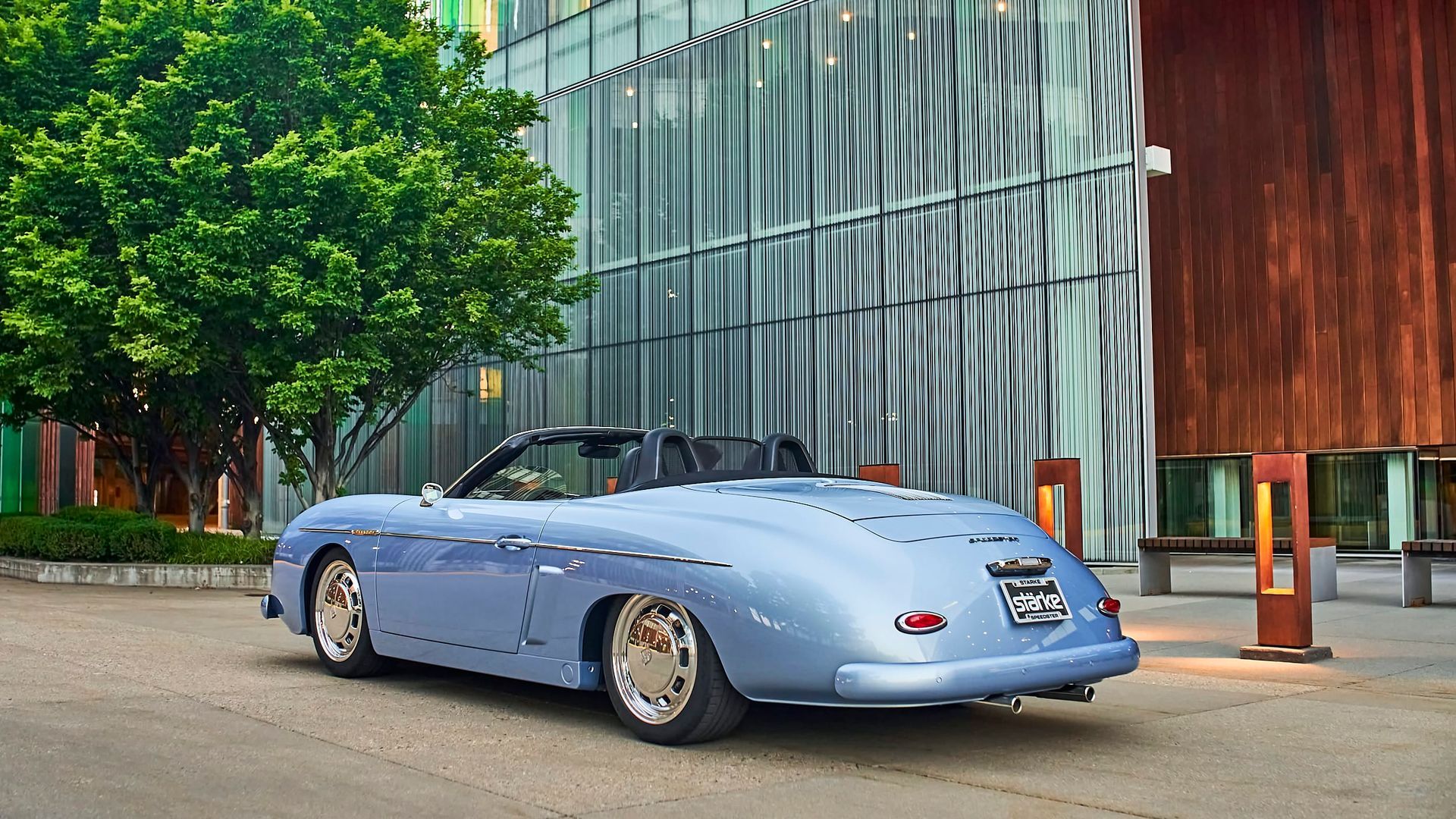 Light blue vintage convertible parked in front of a modern building with glass and wood elements.