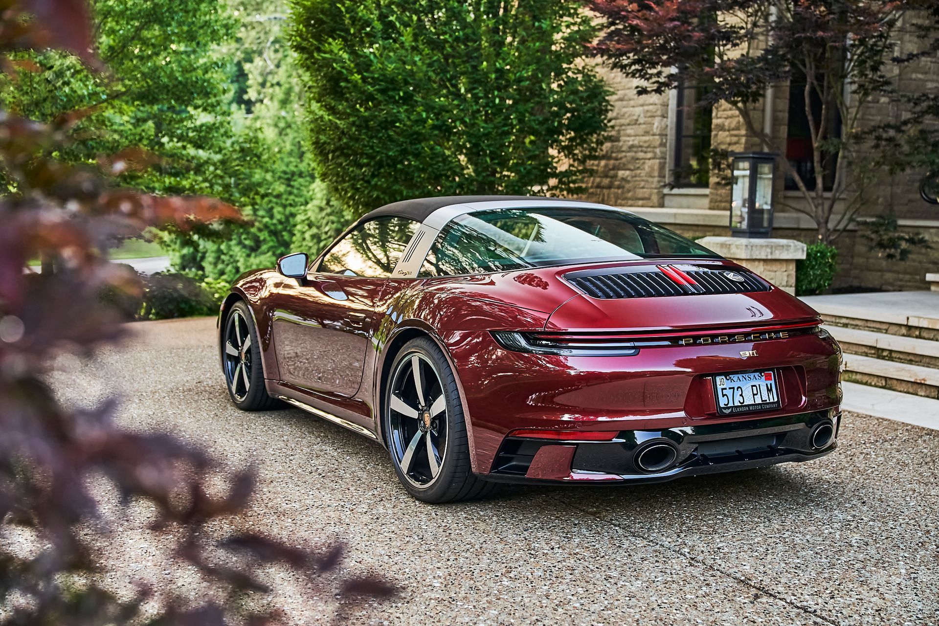 A red porsche targa is parked on a gravel driveway in front of a house.
