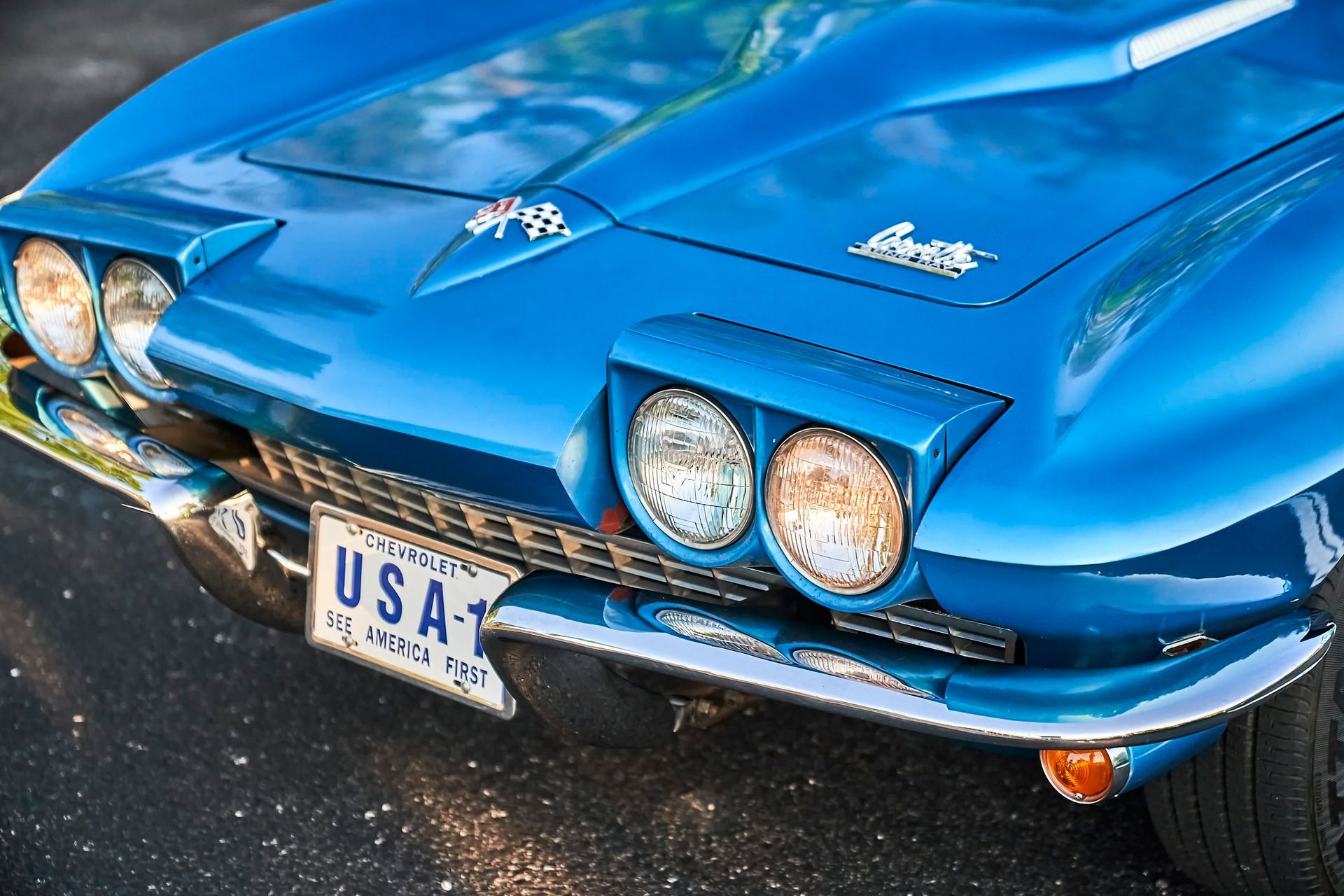 Close-up of a bright blue classic Corvette car, showing the front with headlights and license plate.