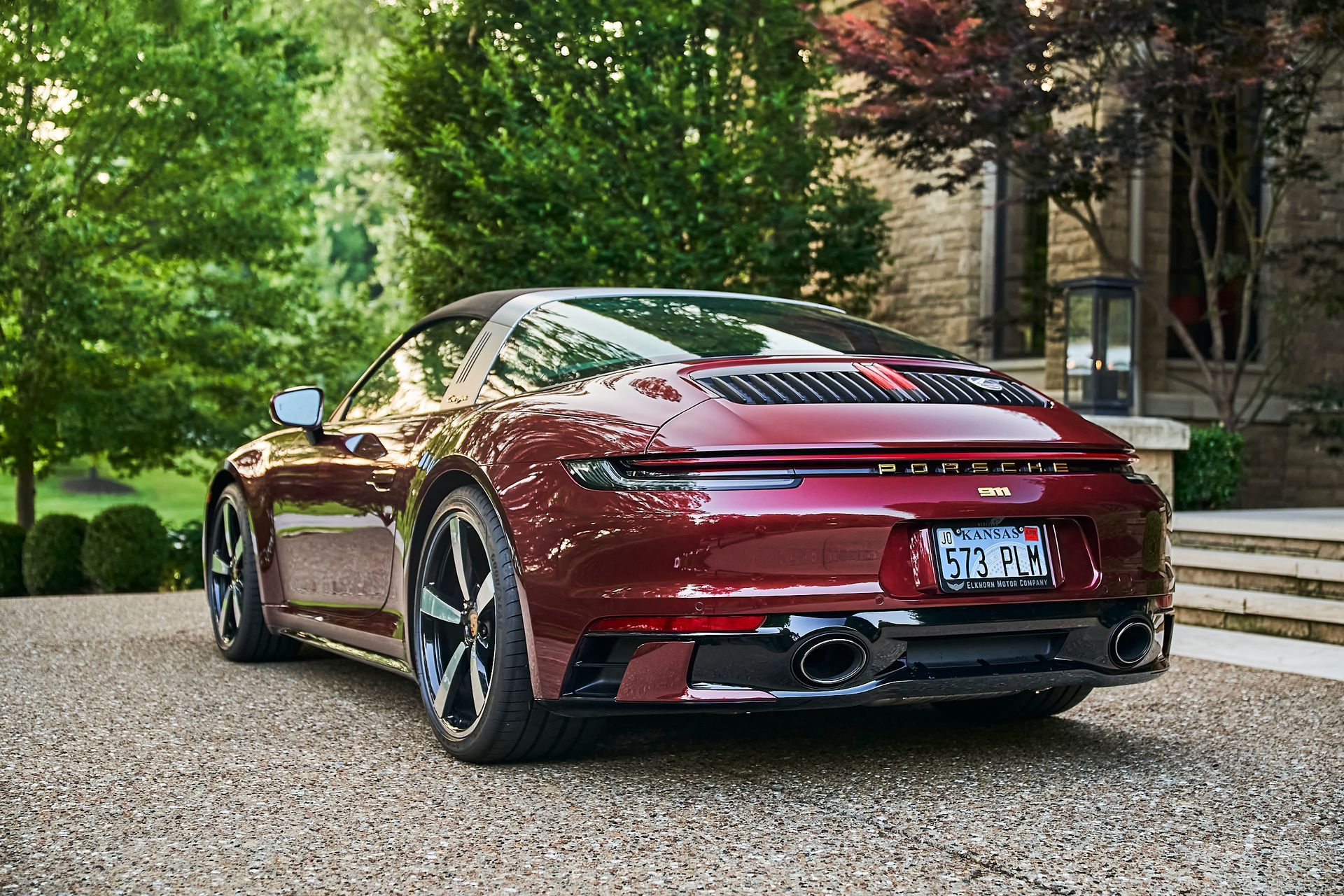 A red porsche 911 is parked on a gravel driveway in front of a house.