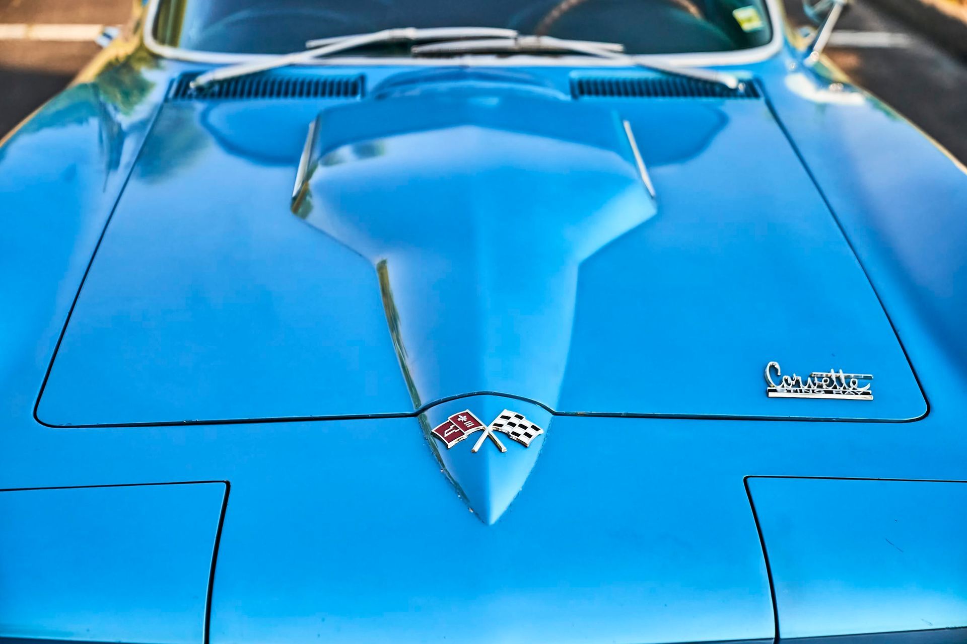 Close-up of a light blue vintage Chevrolet Corvette hood with the Corvette logo and racing flags emblem.