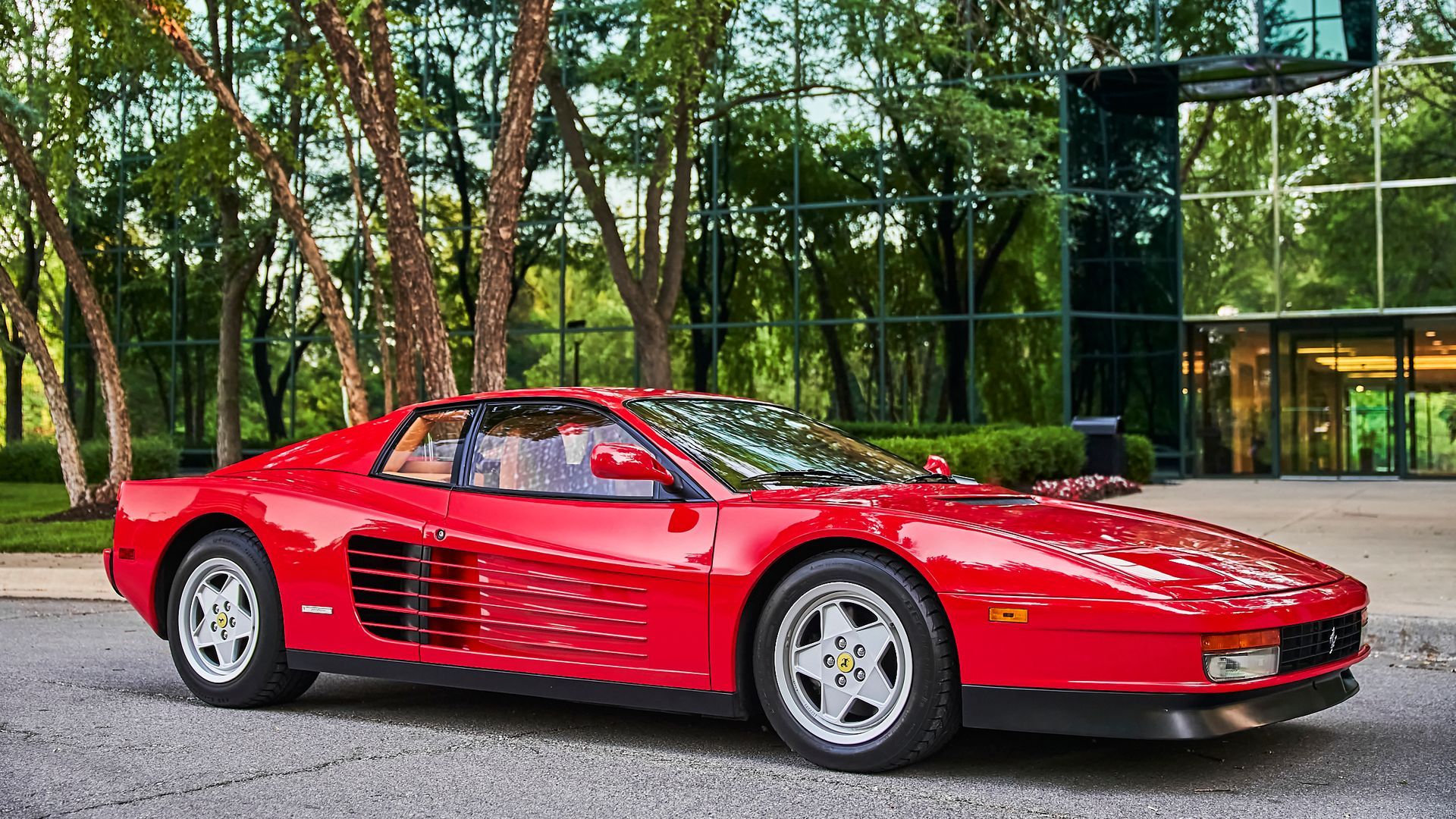 A red ferrari testarossa is parked in front of a building.