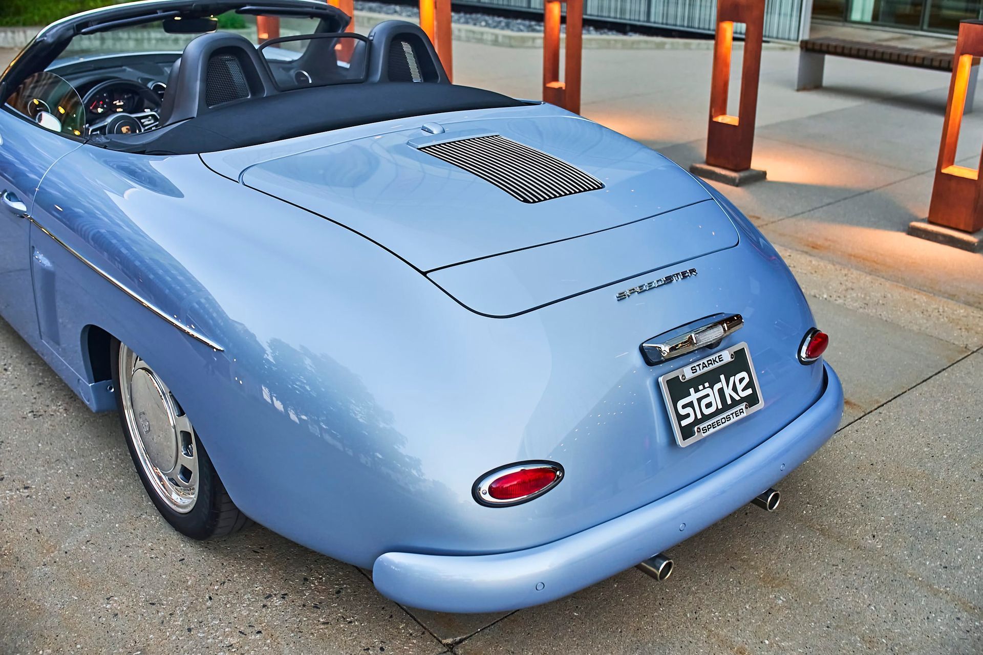 Light blue convertible car parked on a sidewalk. It has a rounded rear end and a black interior.