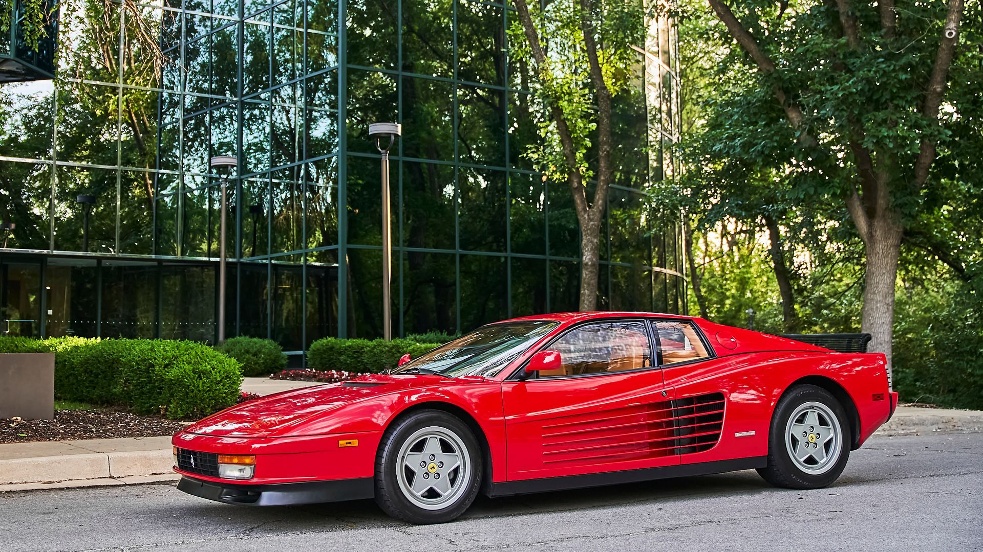 A red ferrari testarossa is parked in front of a building.