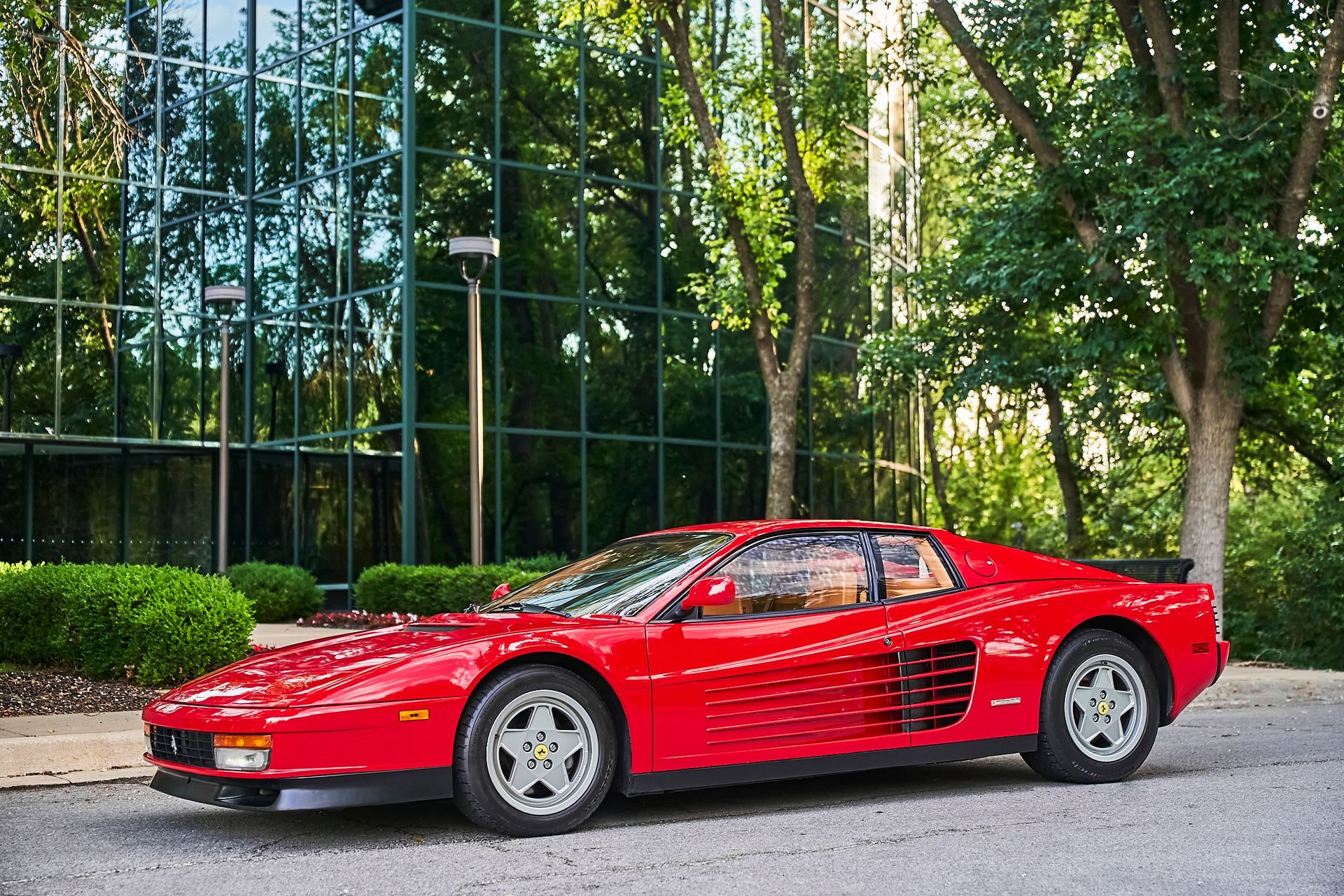 A red ferrari testarossa is parked in front of a building.