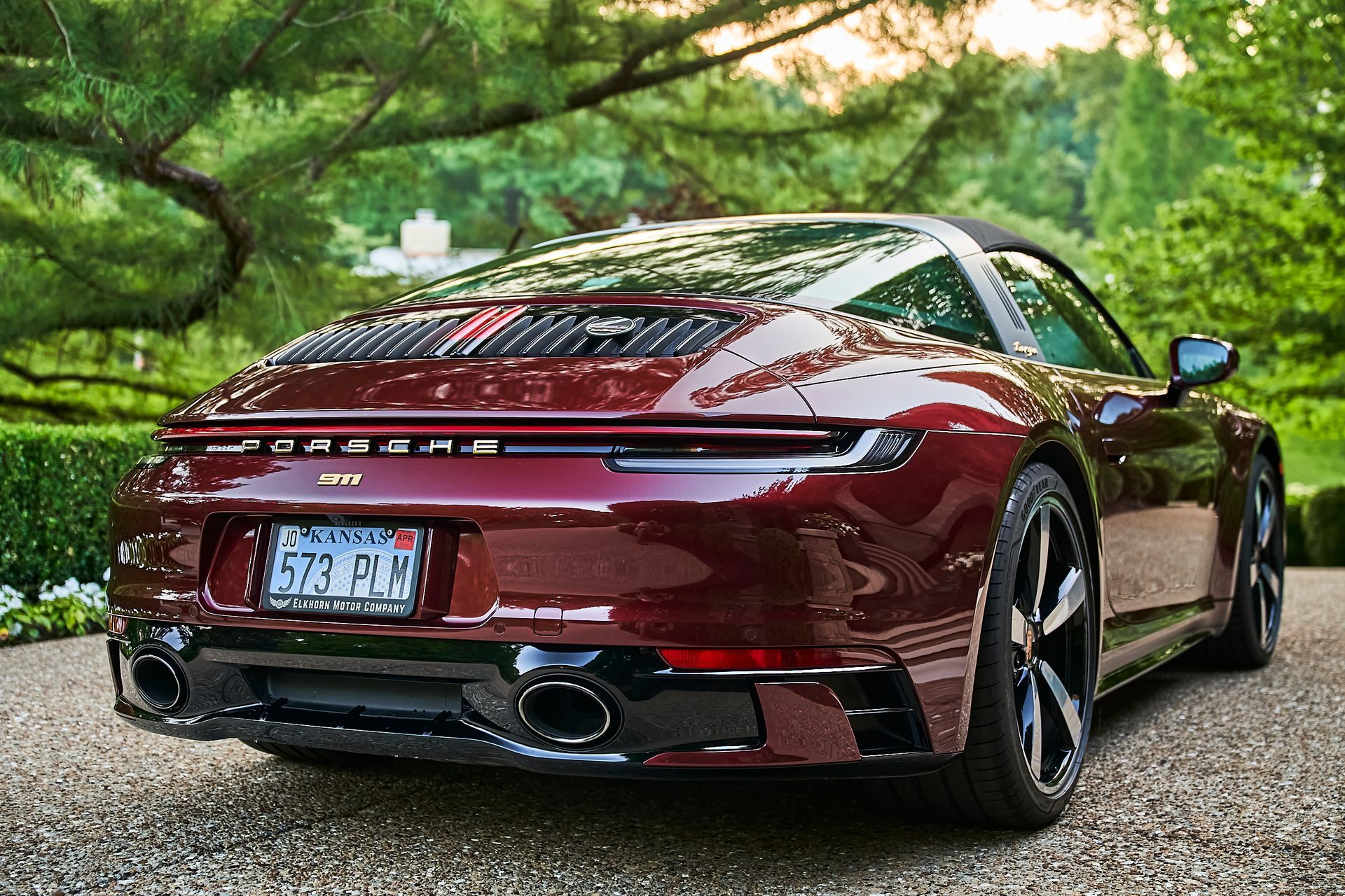 A red porsche 911 targa is parked on a gravel driveway.