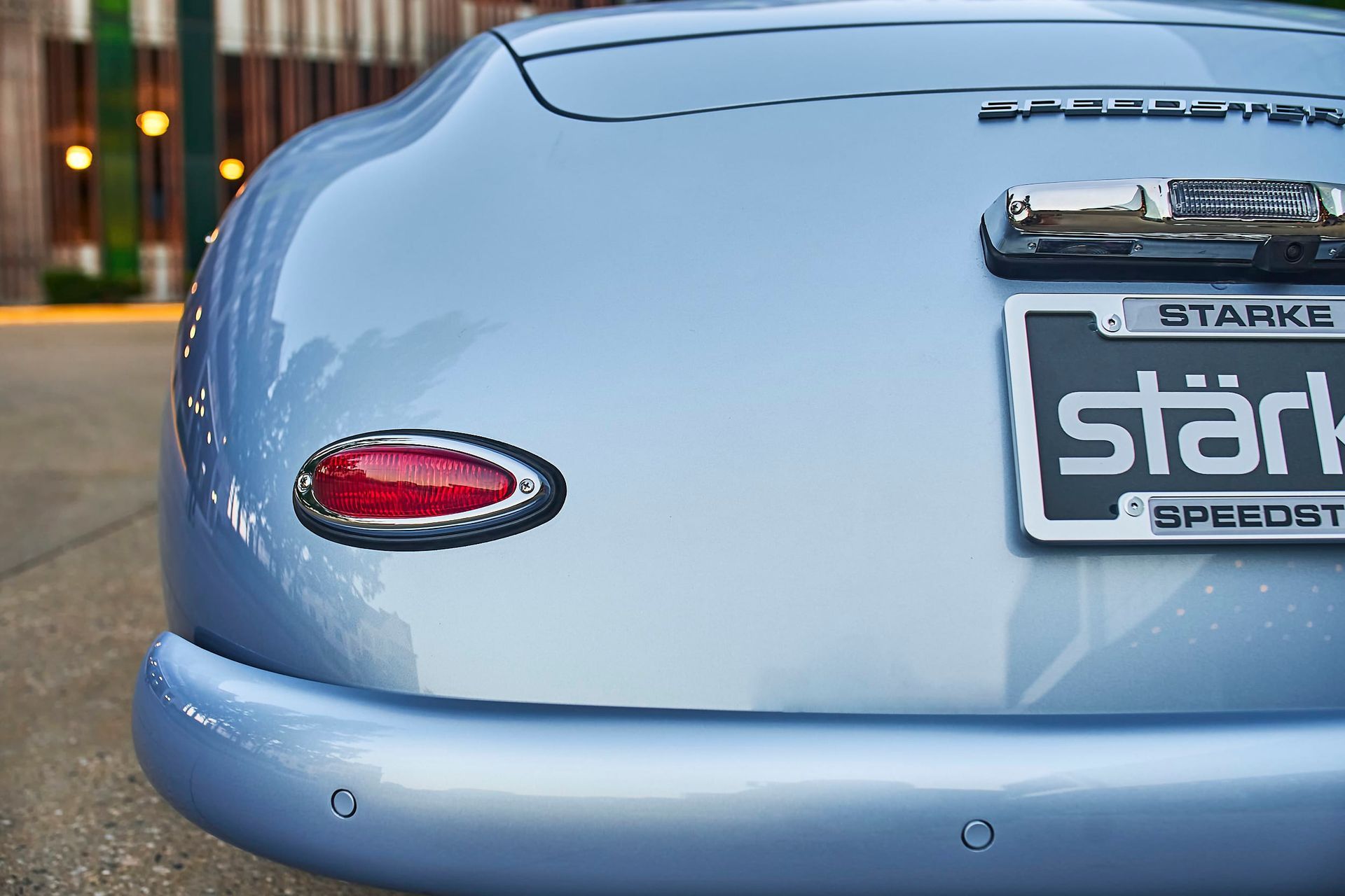 Close-up of a light blue car's rear, showing a red taillight, a Starke license plate, and a chrome accent.
