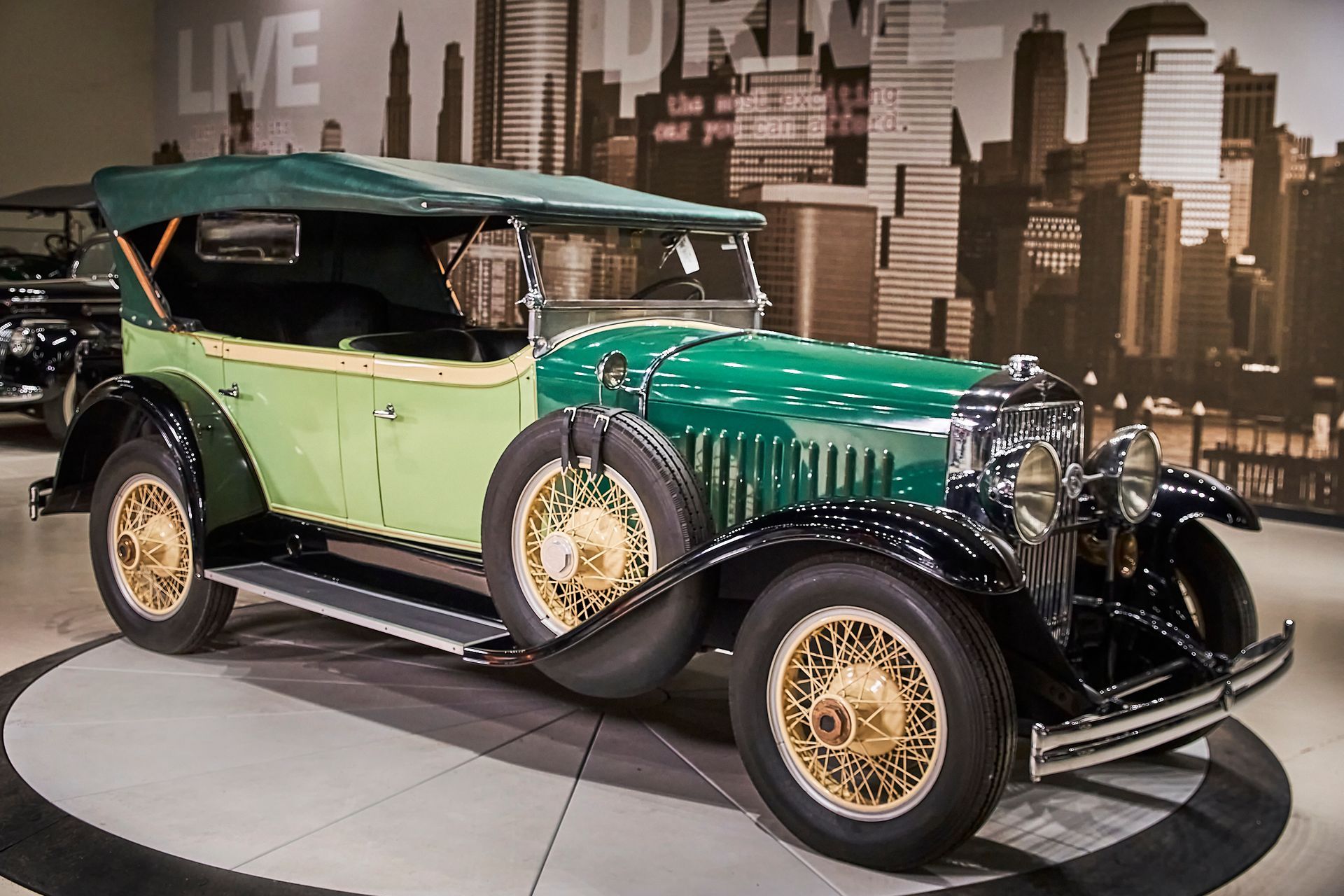 An old green car is parked in front of a live sign