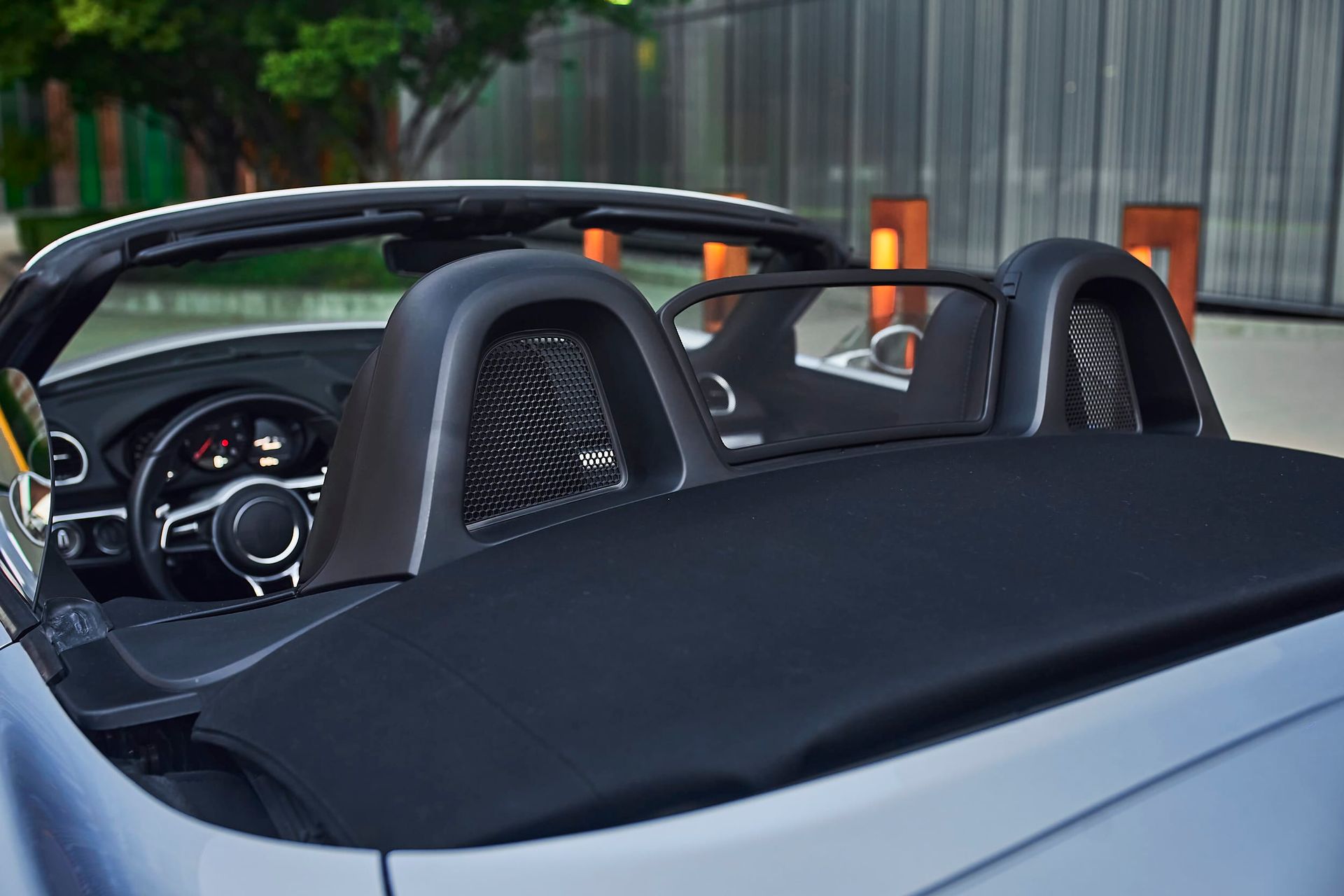 Close-up of the rear of a silver convertible car. The black roof is down, revealing the driver's seat and roll bars.