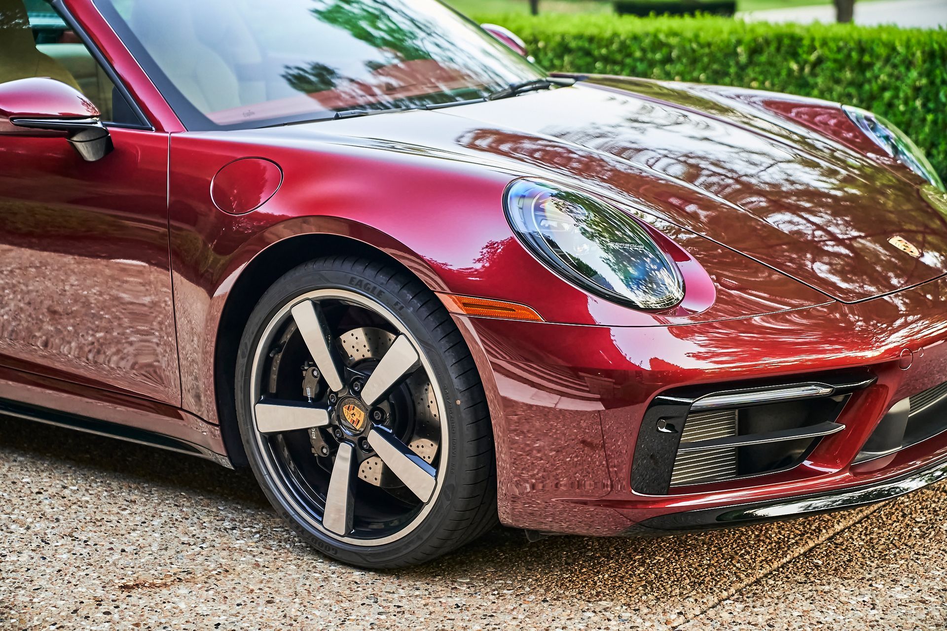 A red porsche 911 is parked on gravel in a driveway.