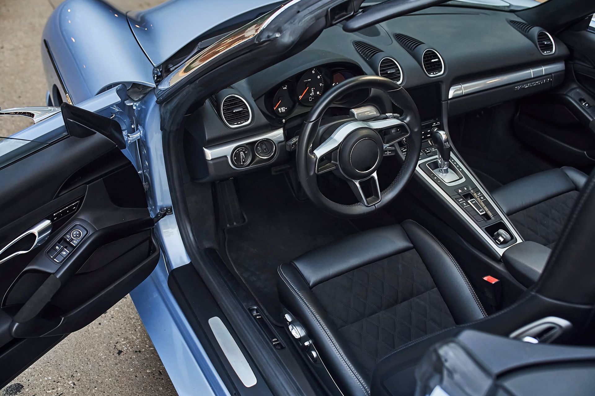 Interior view of a blue convertible sports car. Black leather seats, a black steering wheel, and a dashboard are visible.