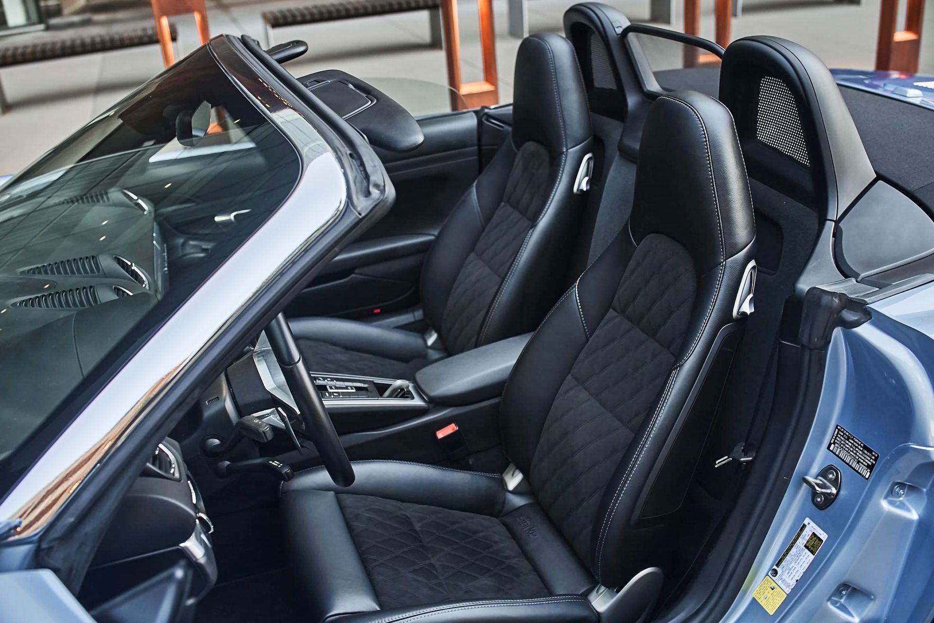 Interior of a blue convertible sports car with black leather seats. Open door reveals driver's seat, steering wheel, and passenger seat.