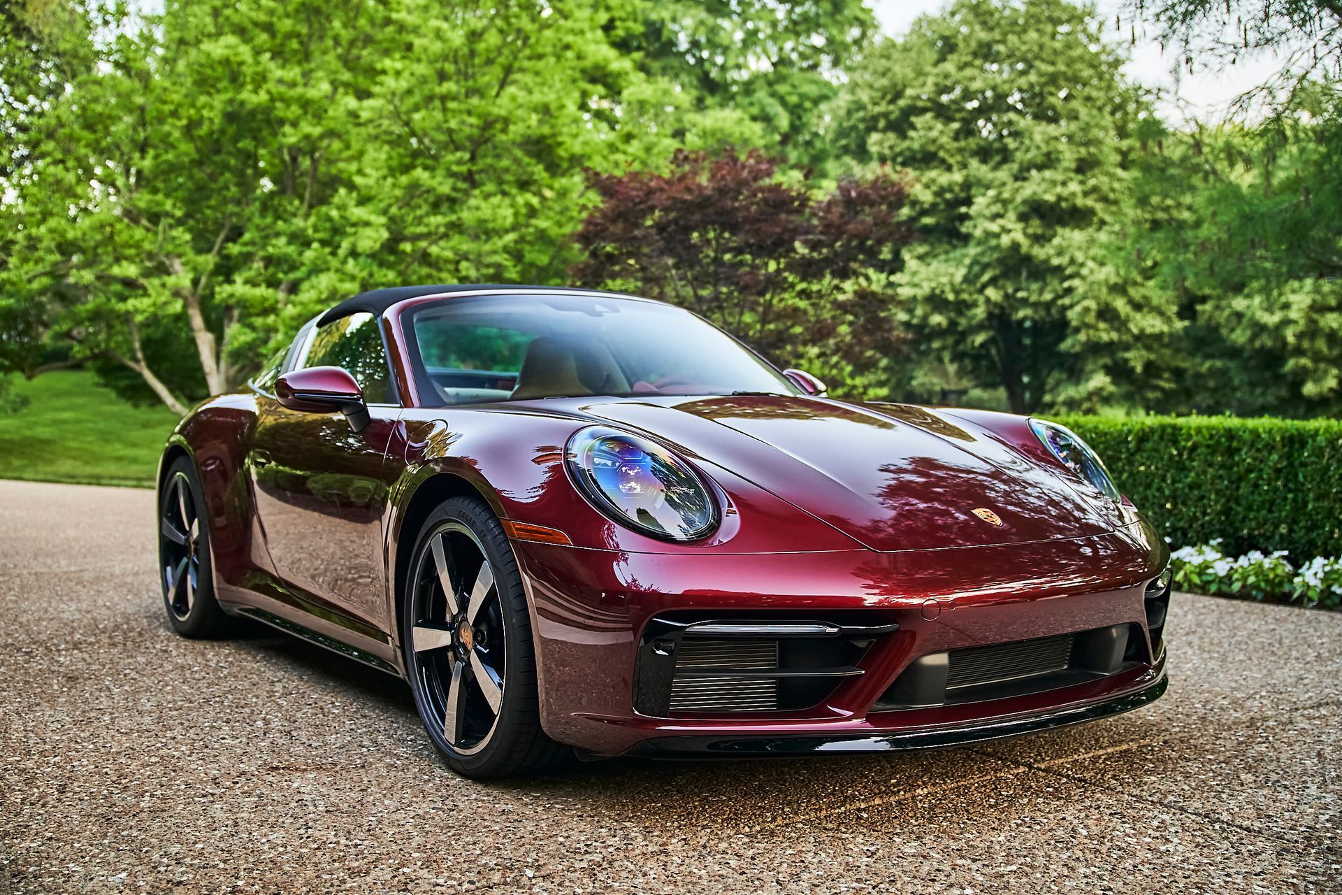 A red porsche 911 targa is parked on a gravel driveway.