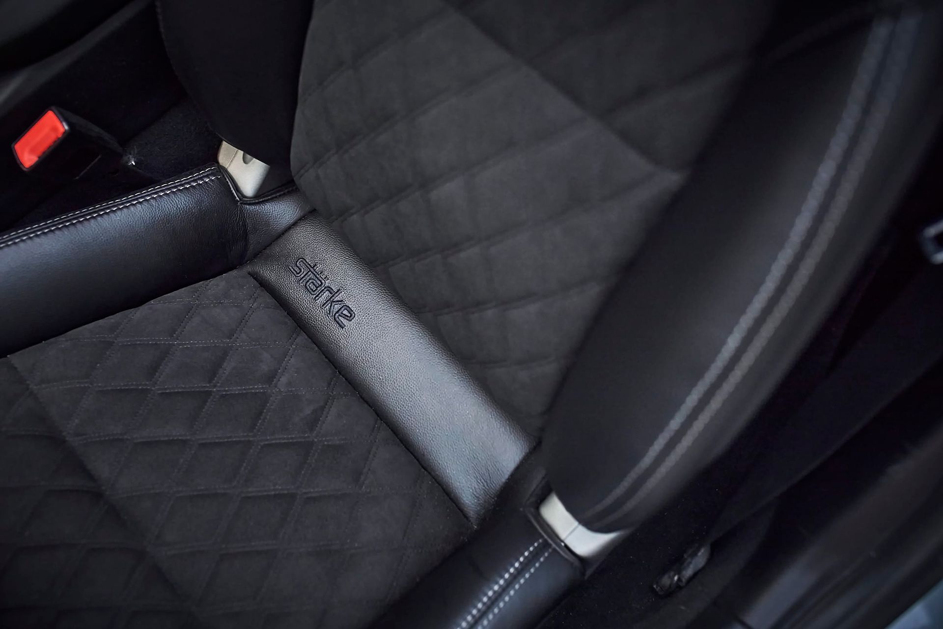 Close-up of a car seat with black quilted suede and leather upholstery, showing wear and damage.